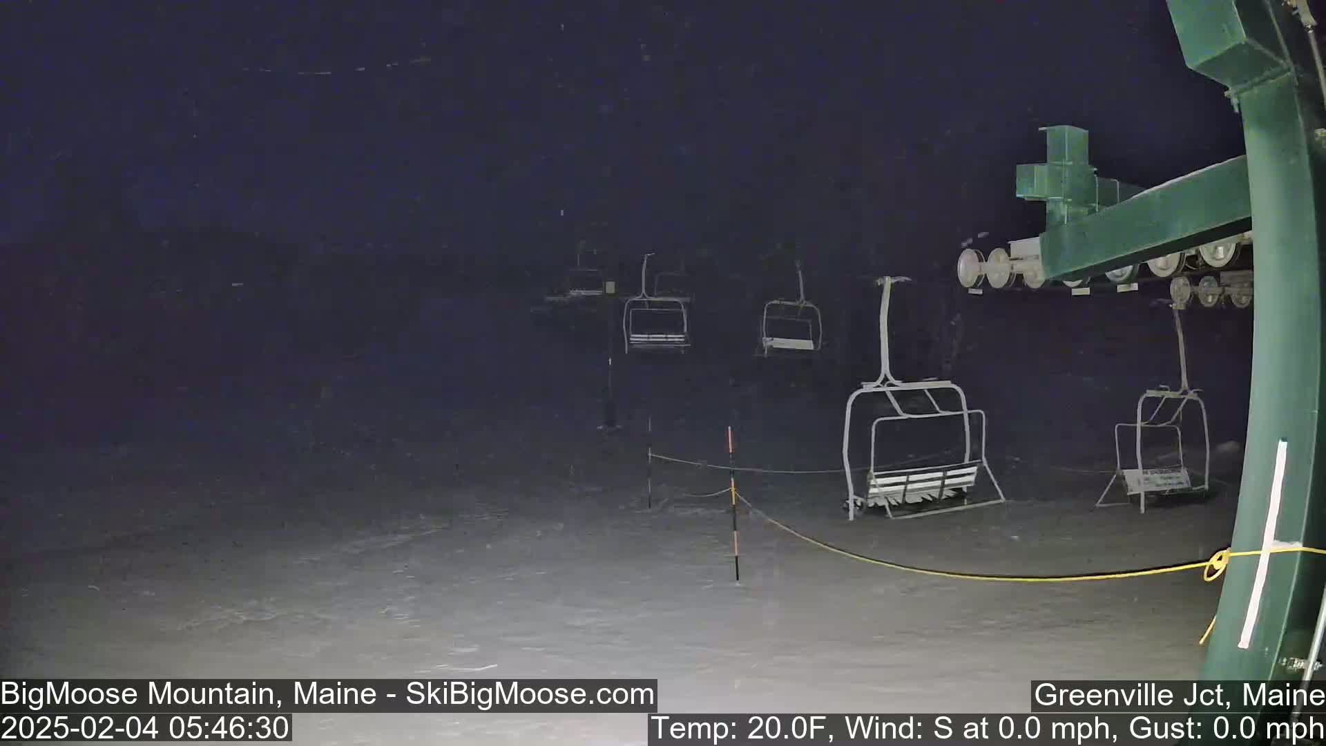 Empty chairlifts sit on a snow-covered ski slope at night during a light snowfall.