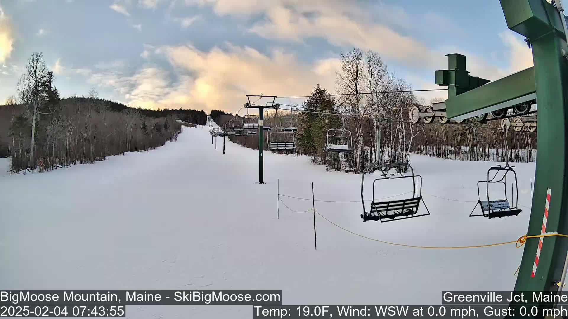 A snow-covered ski slope with several empty chairlifts under a partly cloudy sky.