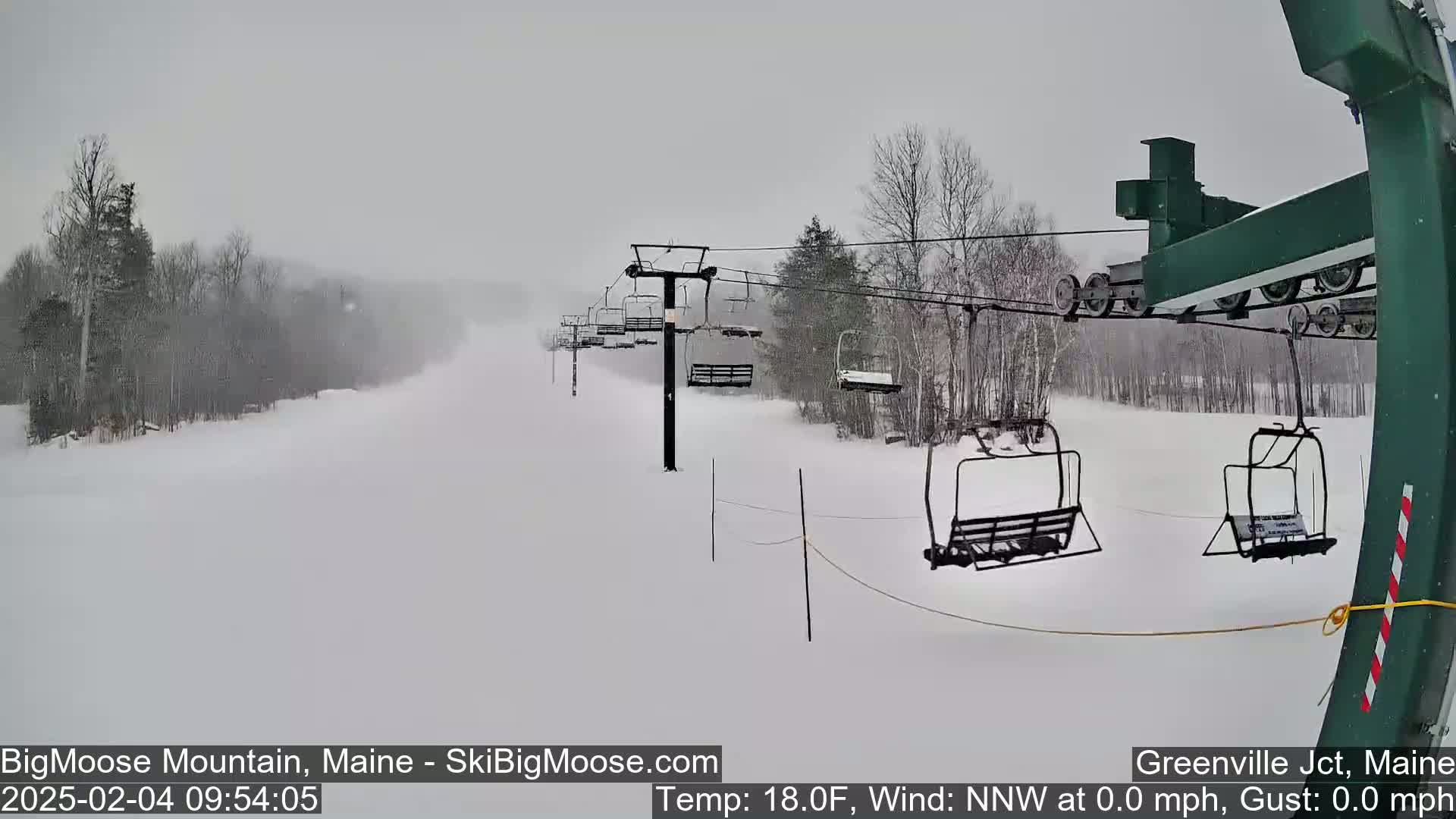 A snow-covered ski slope with a chairlift and sparsely wooded areas is visible in heavy snowfall.