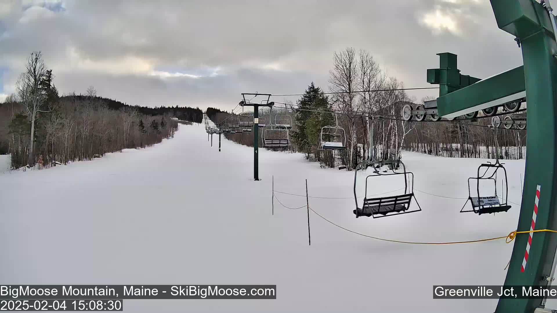 A ski lift with empty chairs ascends a snow-covered slope on an overcast day.
