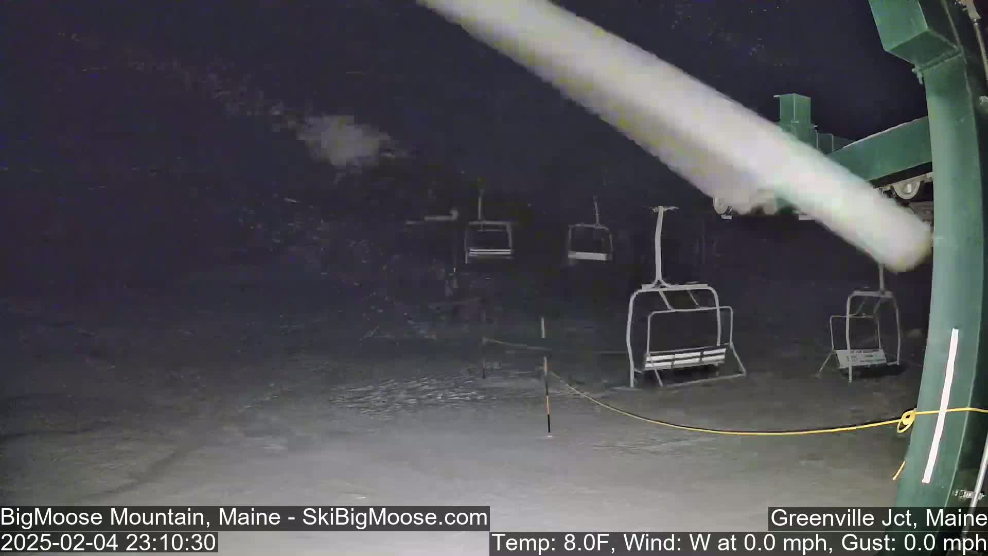 A nighttime view of a snow-covered ski lift with several empty chairs, under calm conditions.