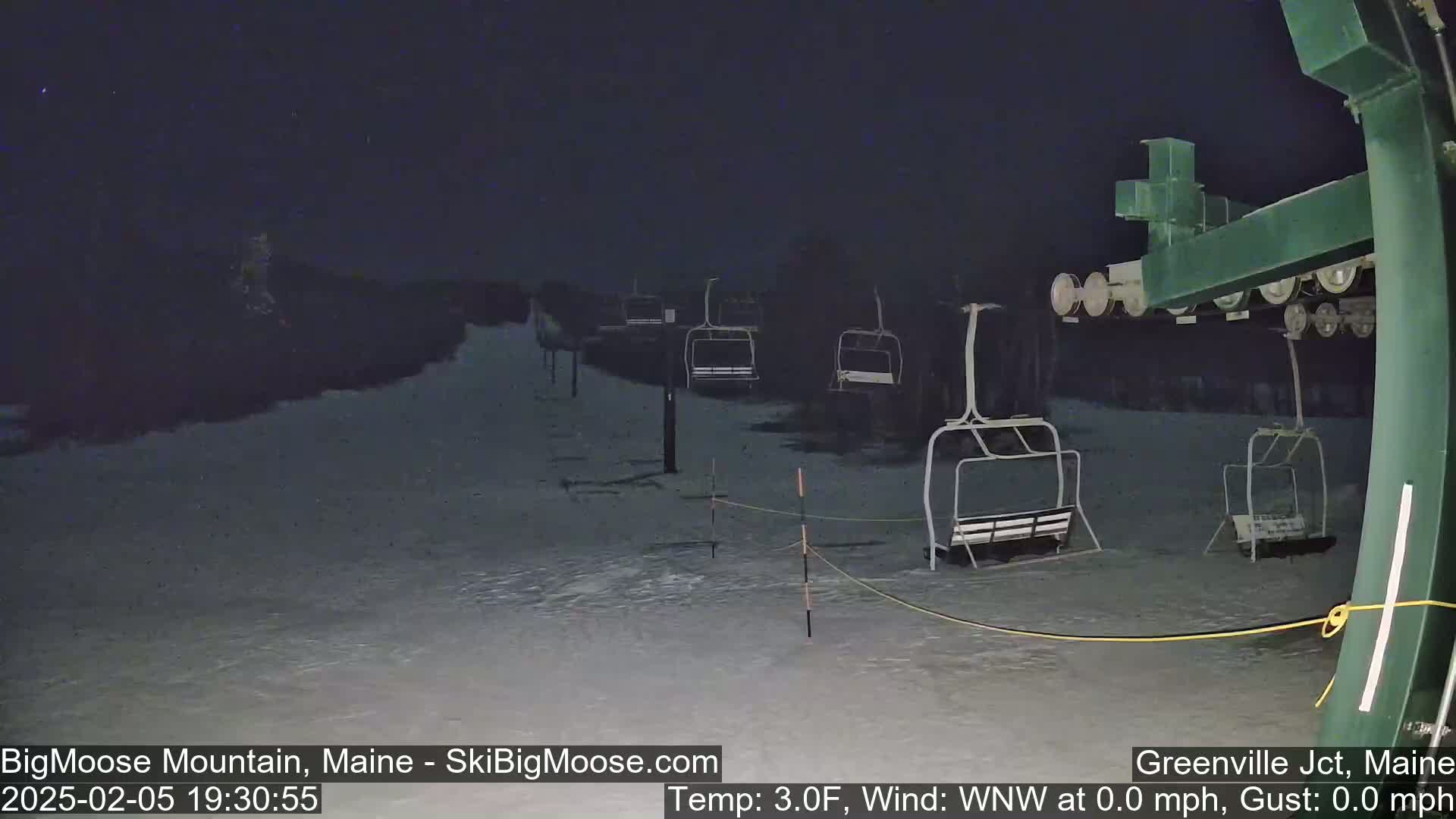 A nighttime view of a snow-covered ski lift with several empty chairs under a dark sky, with a temperature of 3 degrees Fahrenheit and no wind.