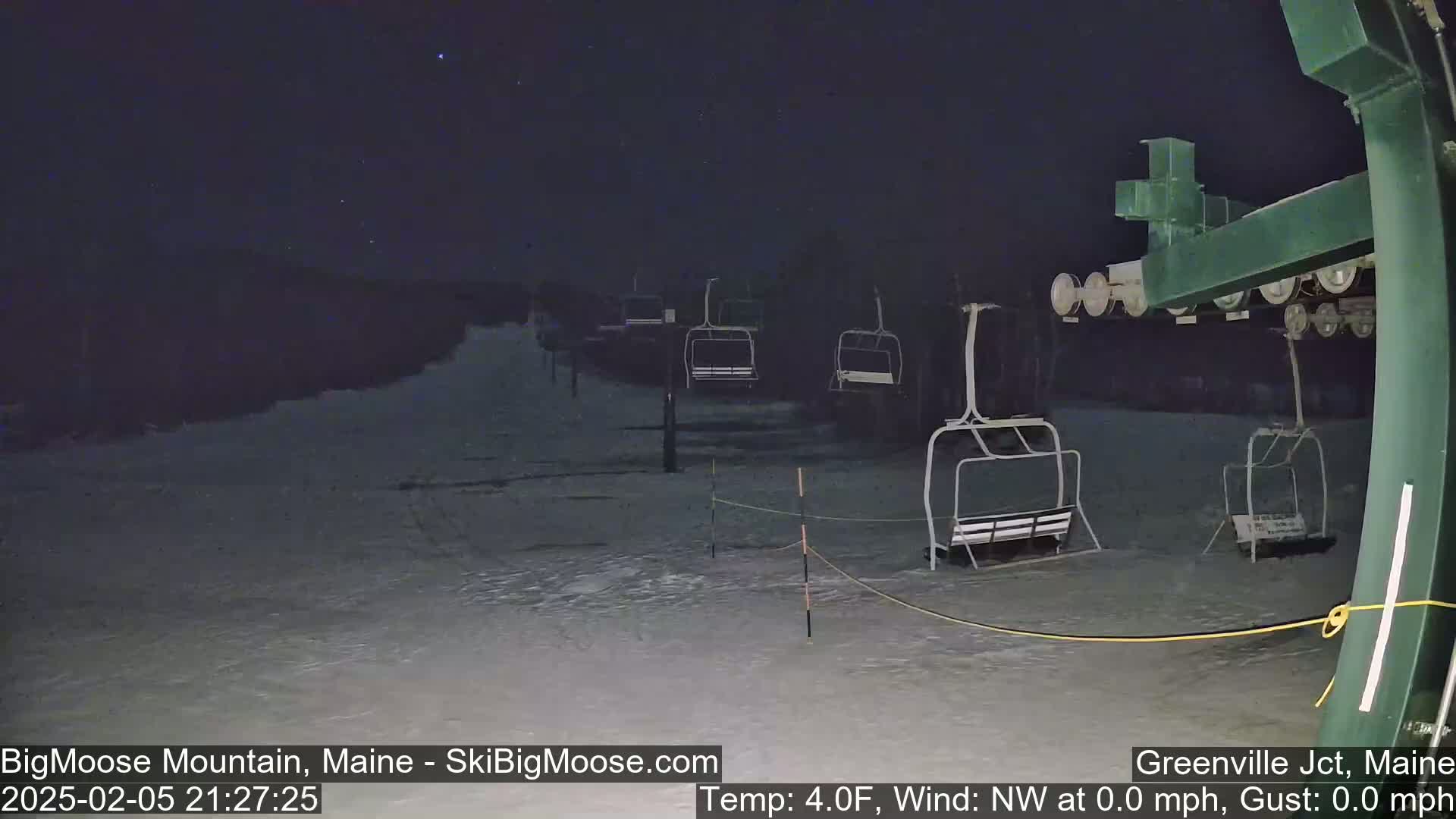A nighttime view of a snow-covered ski lift with several empty chairlifts under a clear, starry sky.