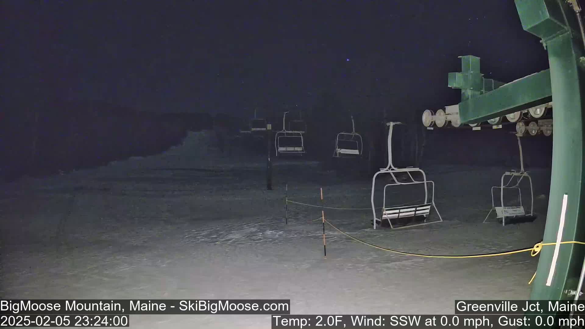 Under a dark, starry night, several empty chairlifts stand on a snow-covered ski slope.