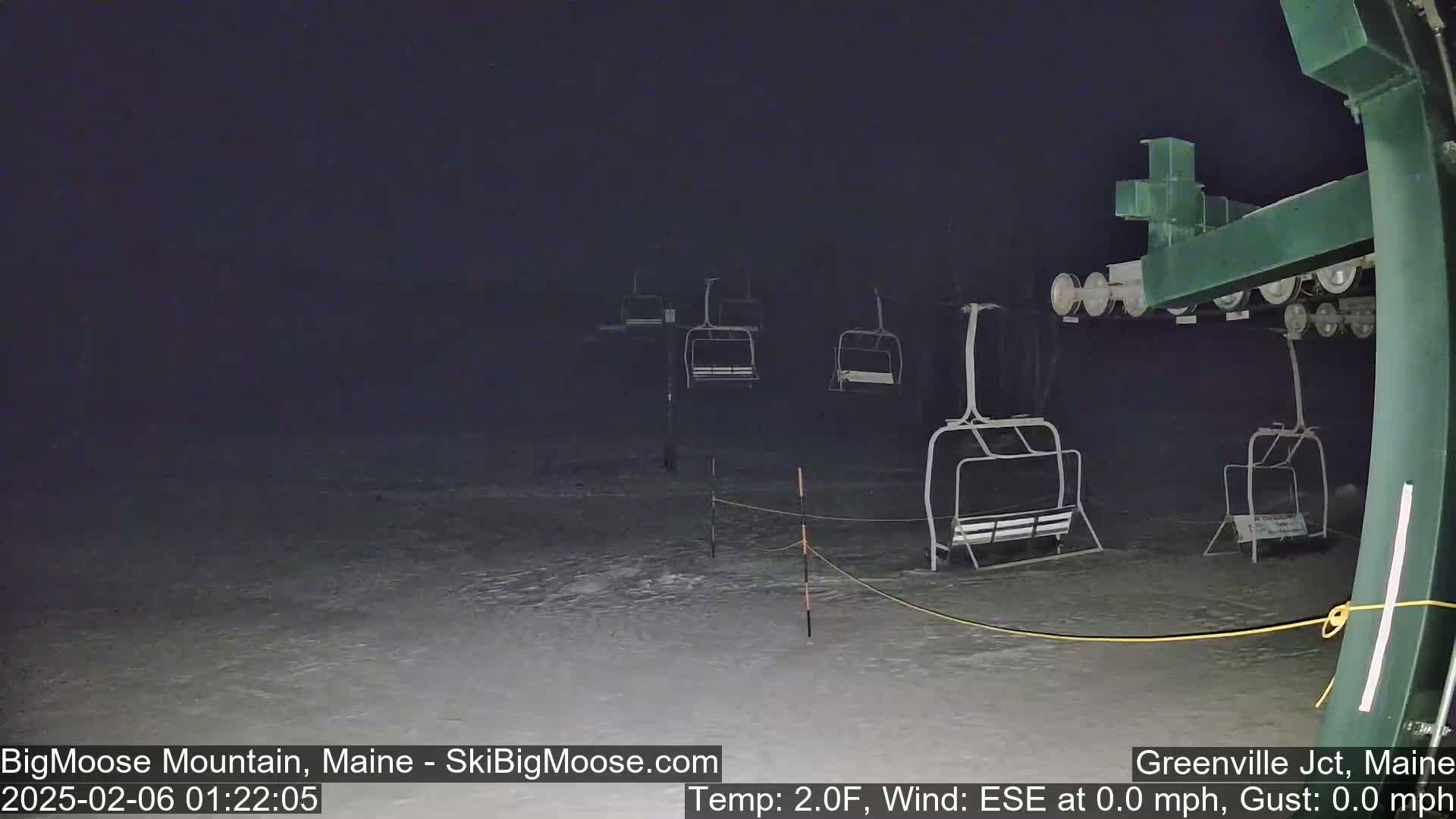 Empty ski lift chairs sit on a snow-covered slope at night under a dark sky.