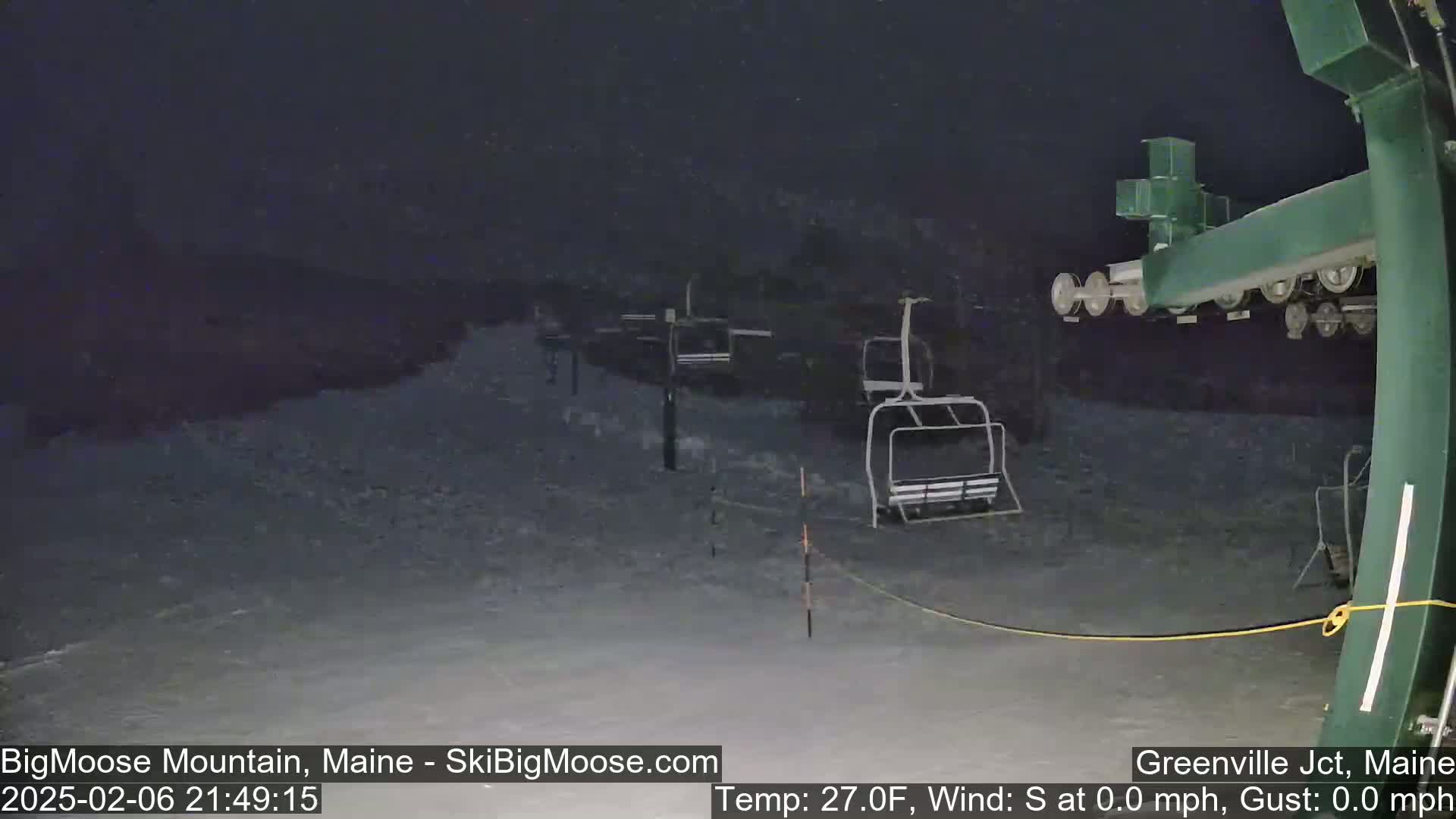 A nighttime snow scene shows several empty ski lifts on a snow-covered slope under a dark, snowy sky.
