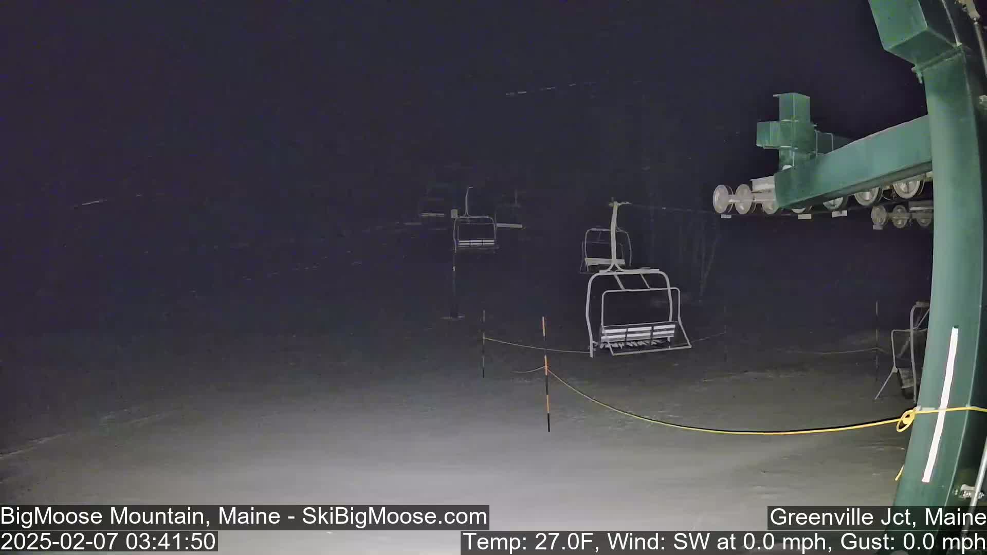 A nighttime view of a snow-covered ski lift with several empty chairlifts under calm, clear conditions.