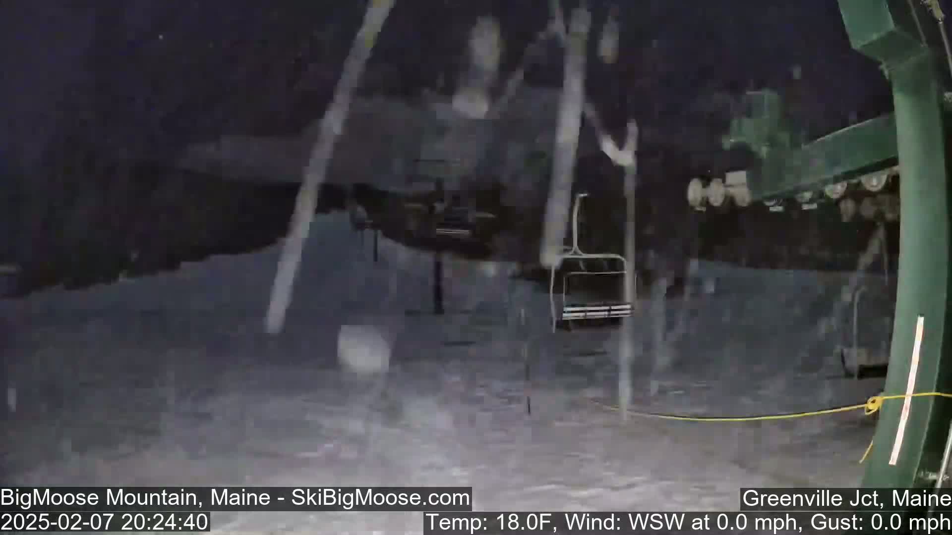 A nighttime snow flurry falls on a ski lift at a snow-covered ski resort.