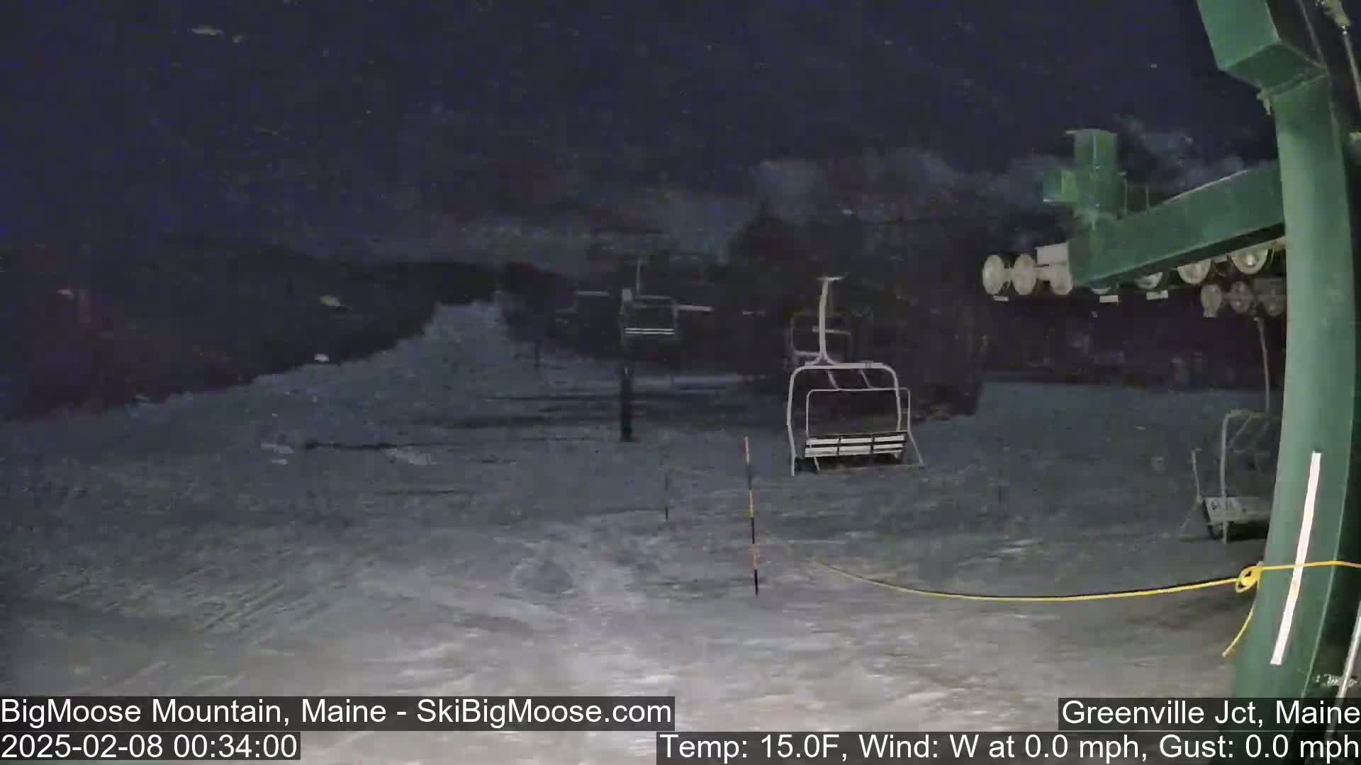 A nighttime, snowy scene shows several empty ski lifts on a snow-covered slope.