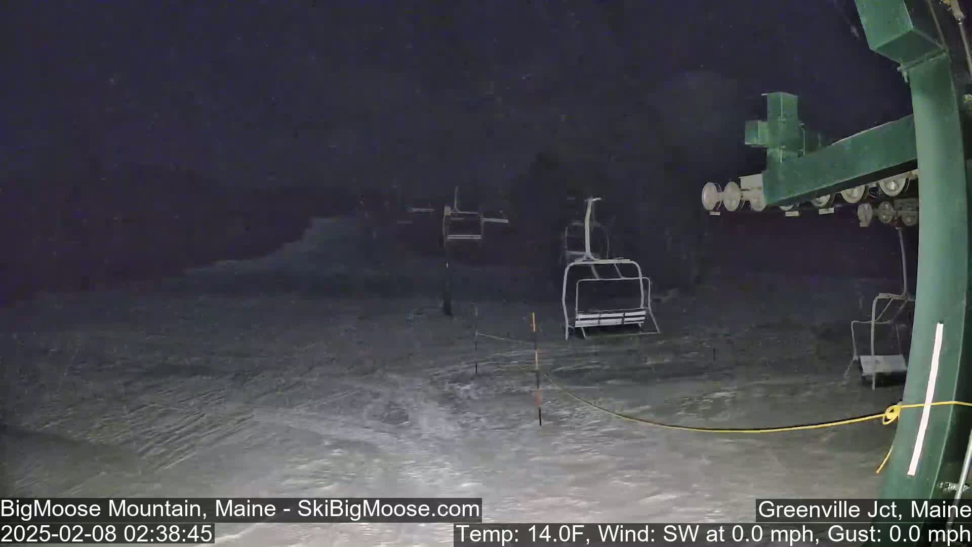 A nighttime view of a snow-covered ski lift with several empty chairlifts, under calm conditions with a temperature of 14 degrees Fahrenheit.