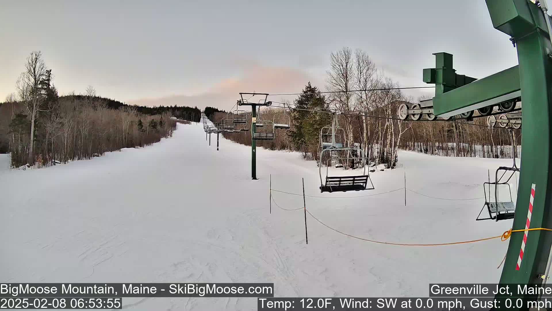 A snow-covered ski slope with several empty chairlifts under a cloudy sky.