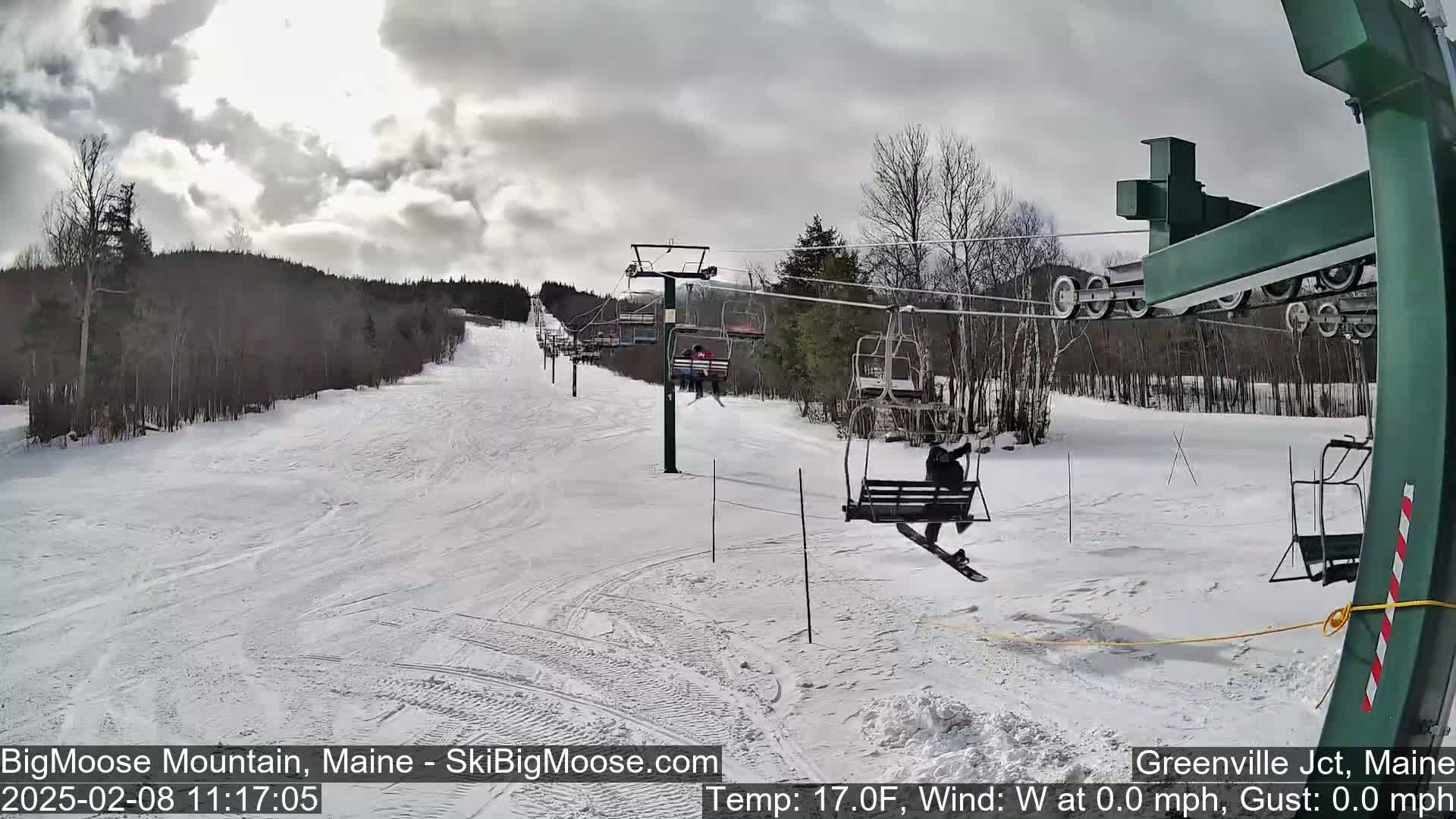 A snowy ski slope with a chairlift and skiers under a cloudy sky.