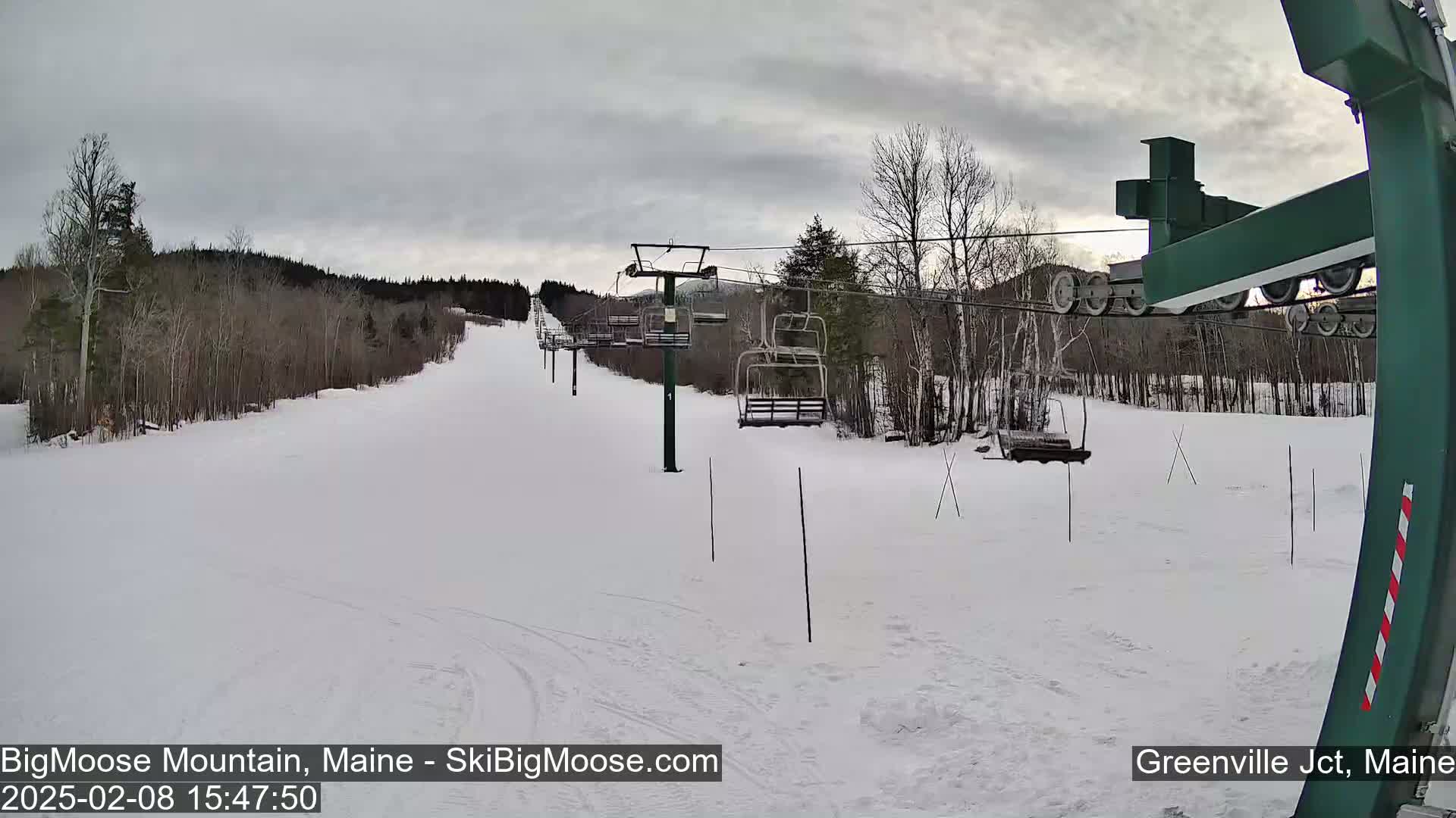 A snow-covered ski slope with a chairlift and bare trees under an overcast sky.