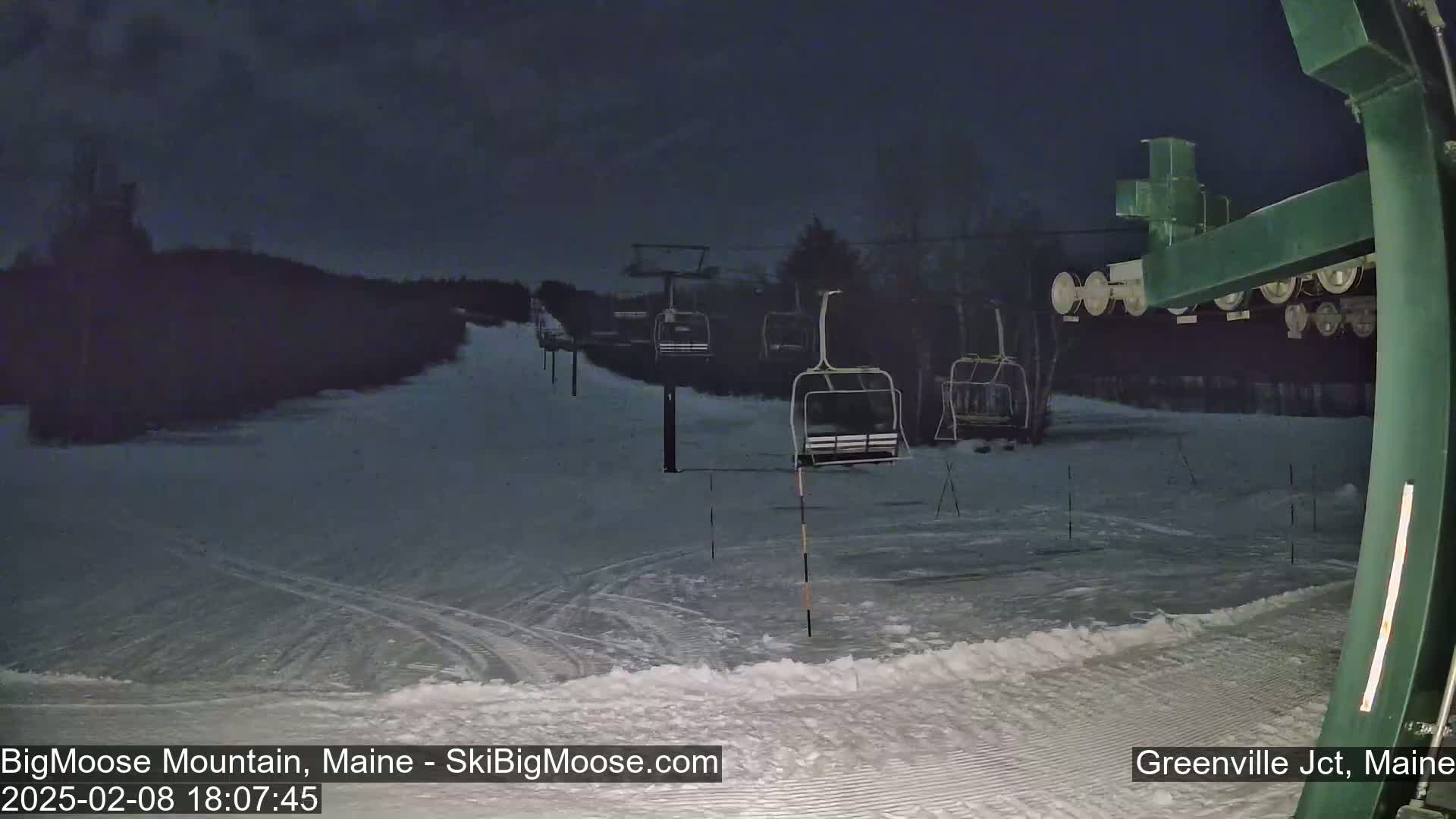 A snow-covered ski slope at night, illuminated by faint light, shows several empty chairlifts under a dark sky.