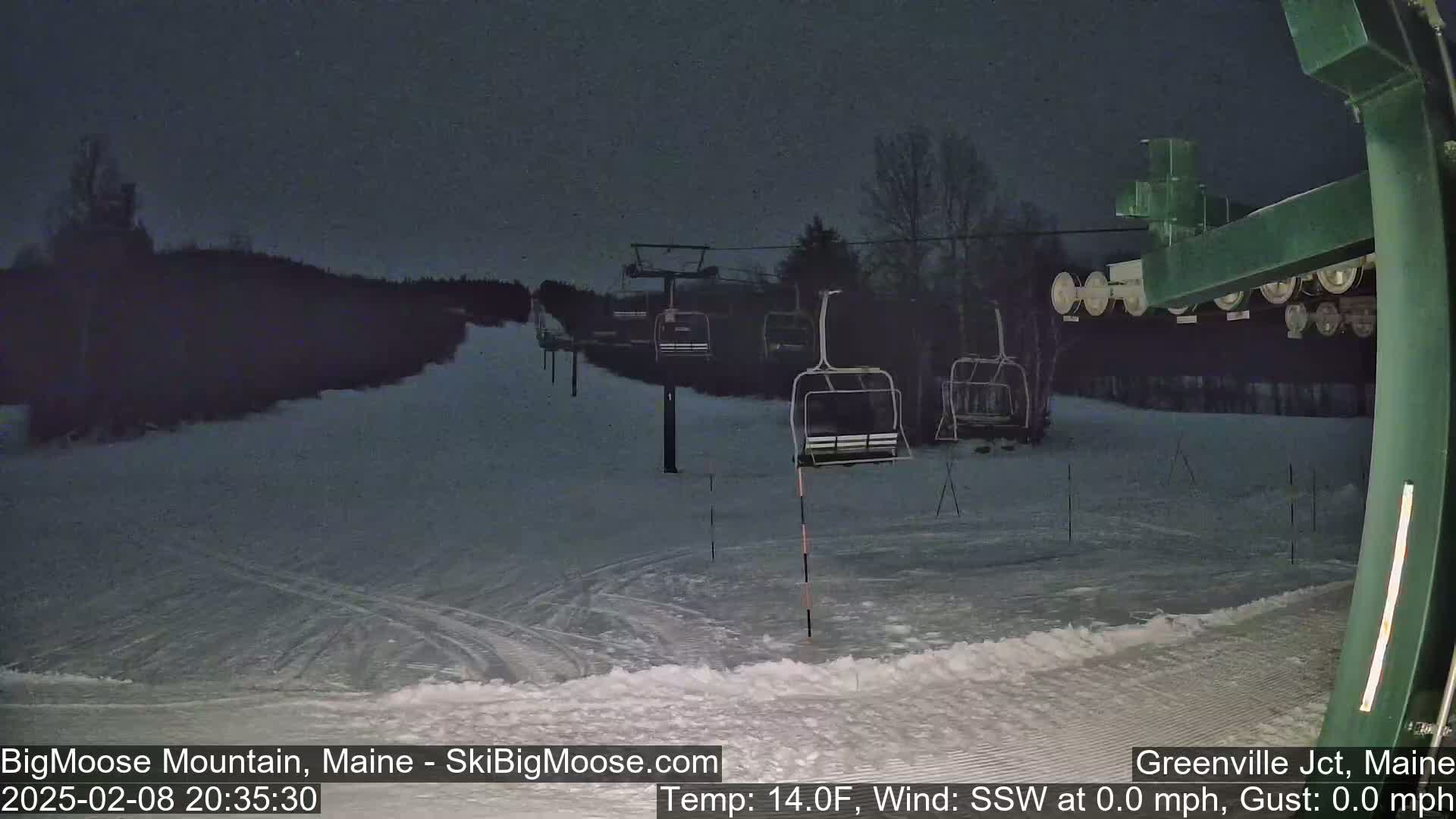 A nighttime view of a snow-covered ski slope with several empty chairlifts under a dark sky.