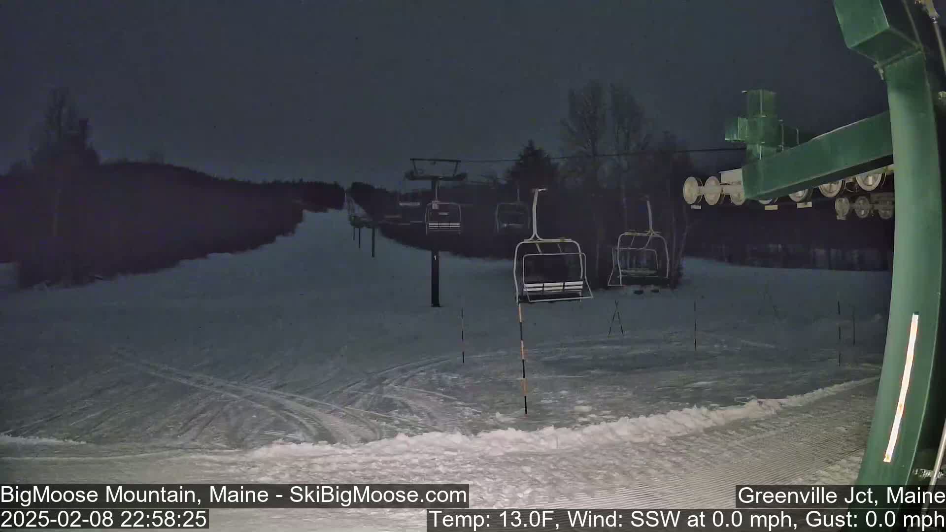 A snow-covered ski slope at night with several empty chairlifts visible under a dark sky.