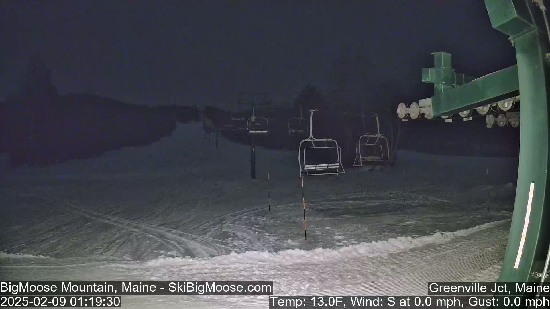 A nighttime view of a snow-covered ski slope with empty chairlifts under a dark sky.