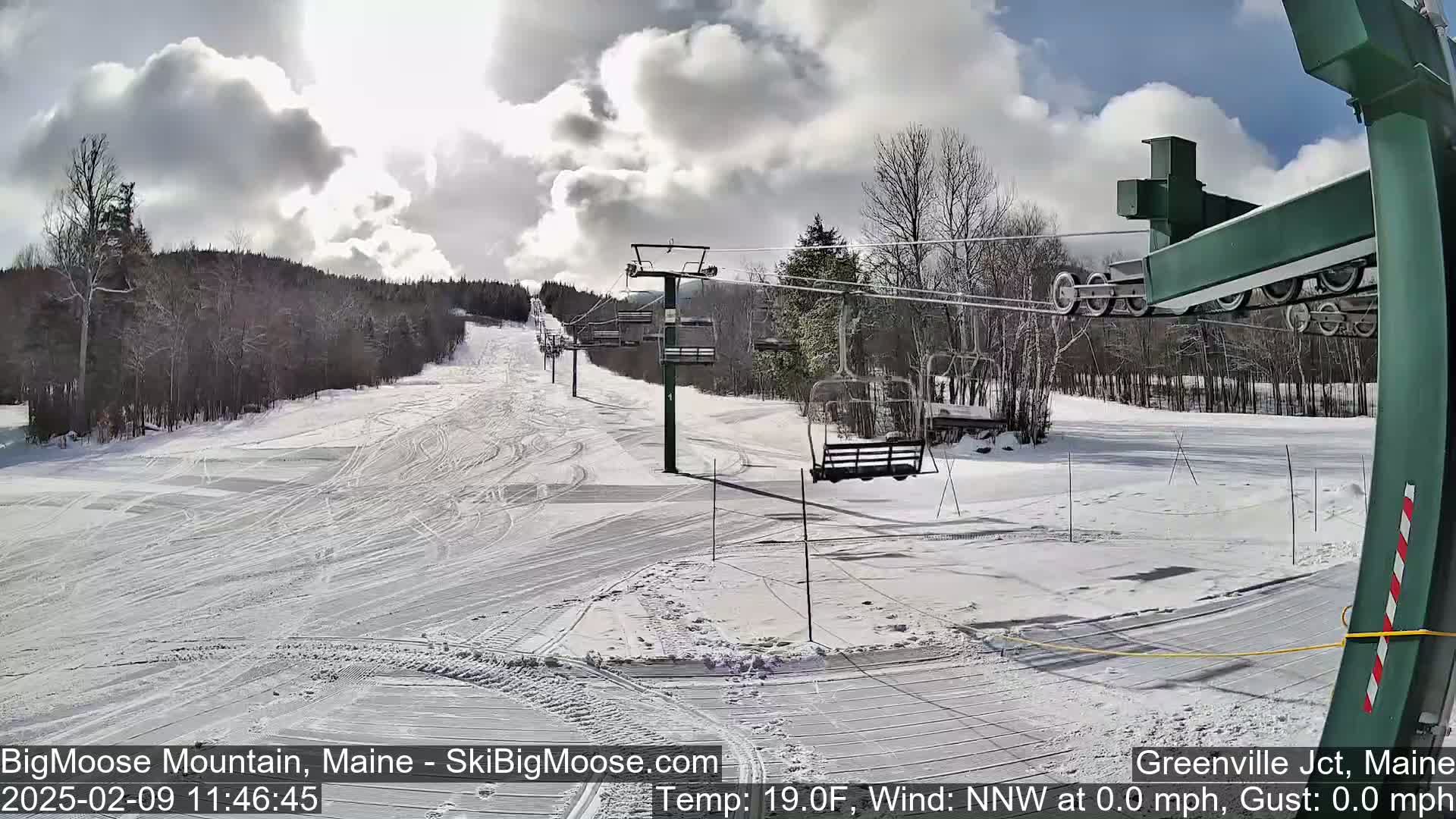 A snow-covered ski slope with a chairlift under a partly sunny sky.
