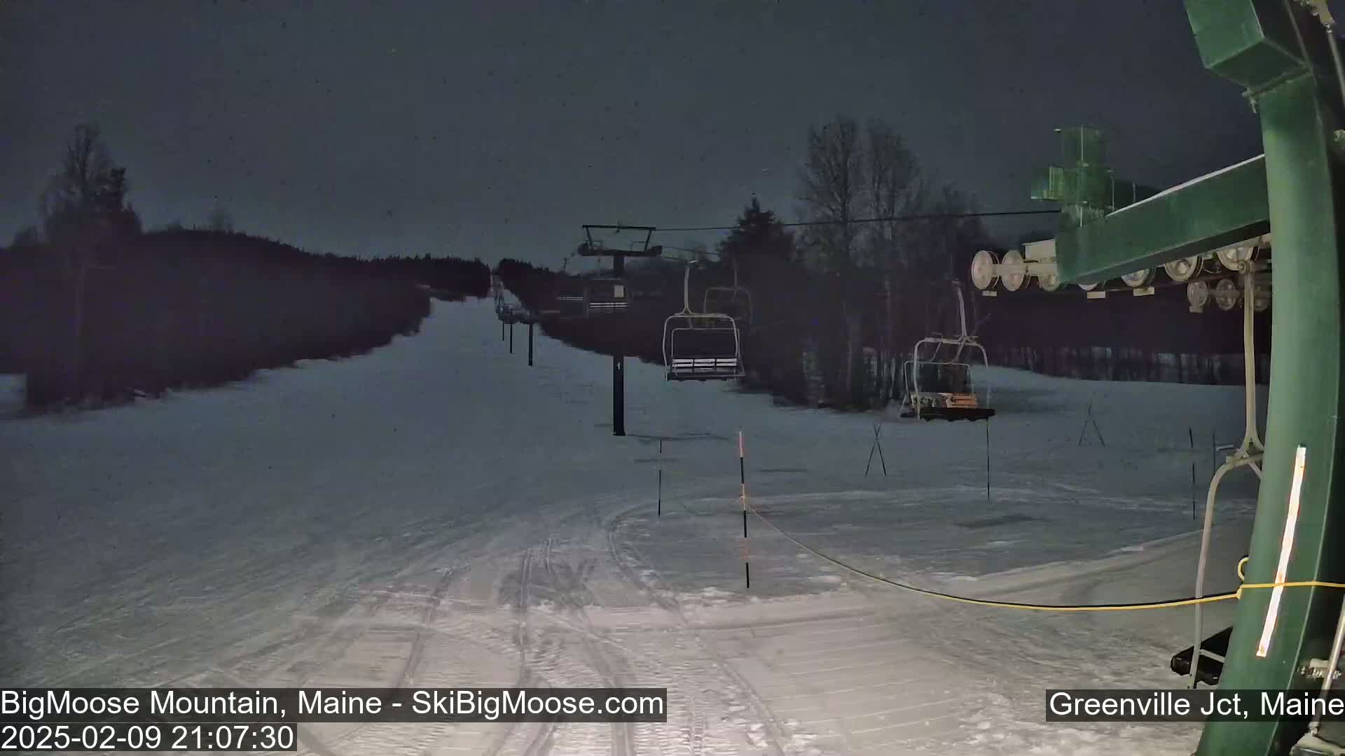 A snow-covered ski slope at night with a chairlift and several ski lifts visible under a dark sky.