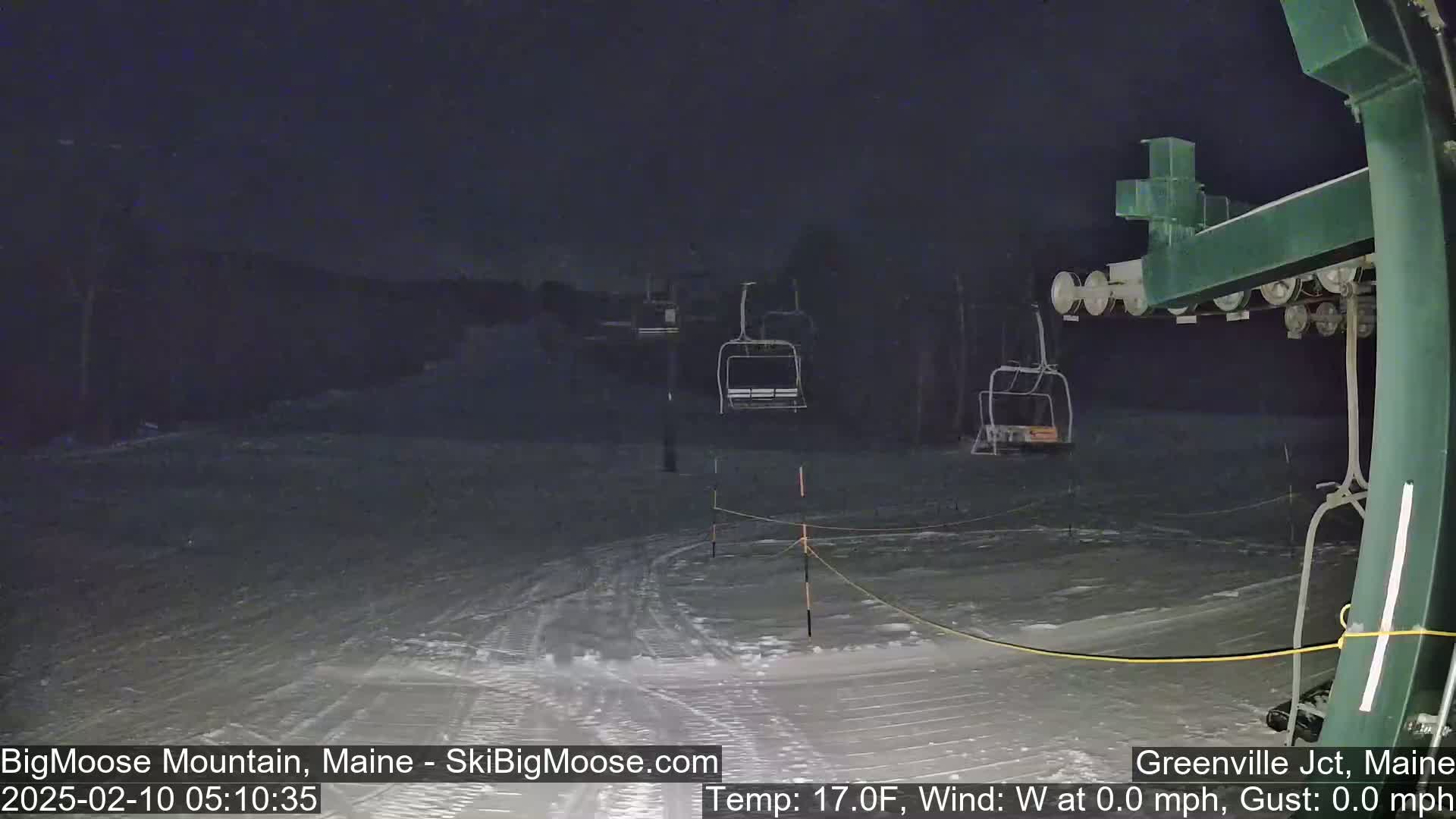 A nighttime view of a snow-covered ski slope with empty chairlifts under a dark sky.