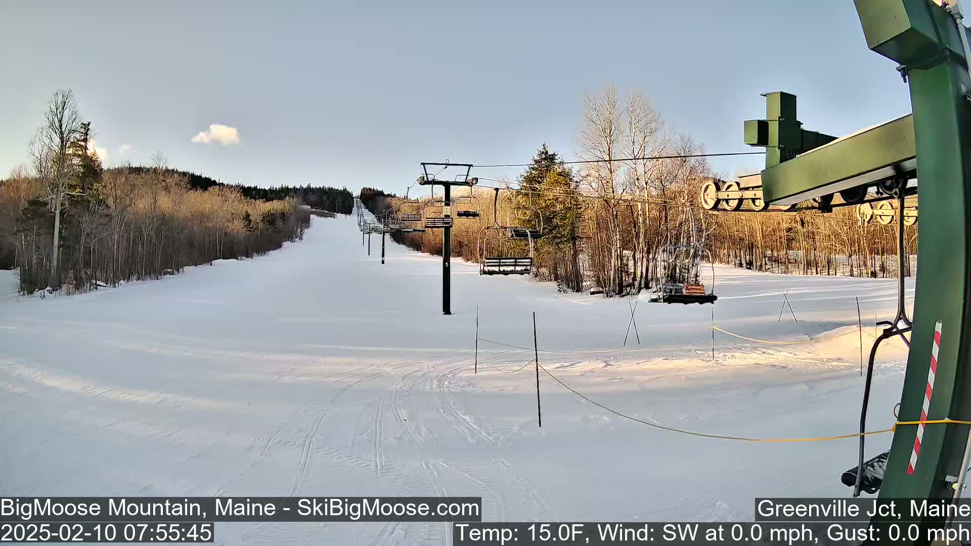 A ski lift ascends a snow-covered hill under a clear, bright sky.