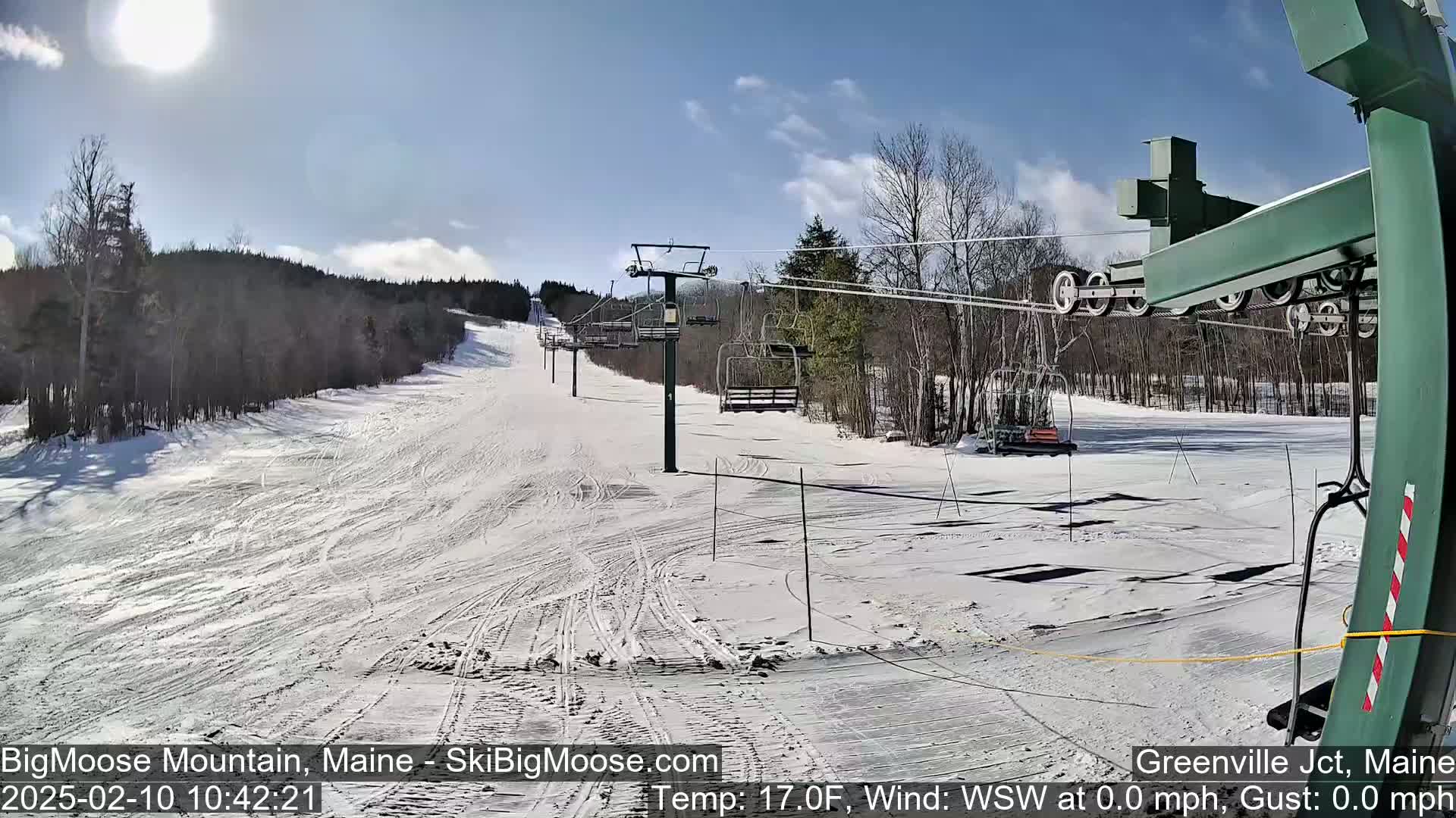 A sunny day at a snow-covered ski resort shows a chairlift and groomed ski runs.
