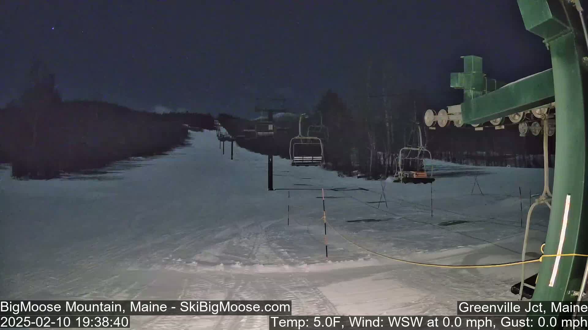 A nighttime view of a snow-covered ski slope with a chairlift under a dark sky.