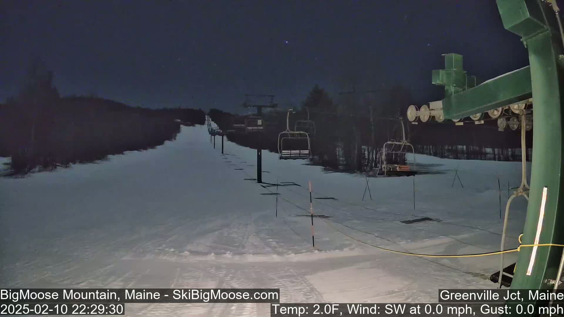 A snow-covered ski slope at night with several empty chairlifts under a clear, starry sky.