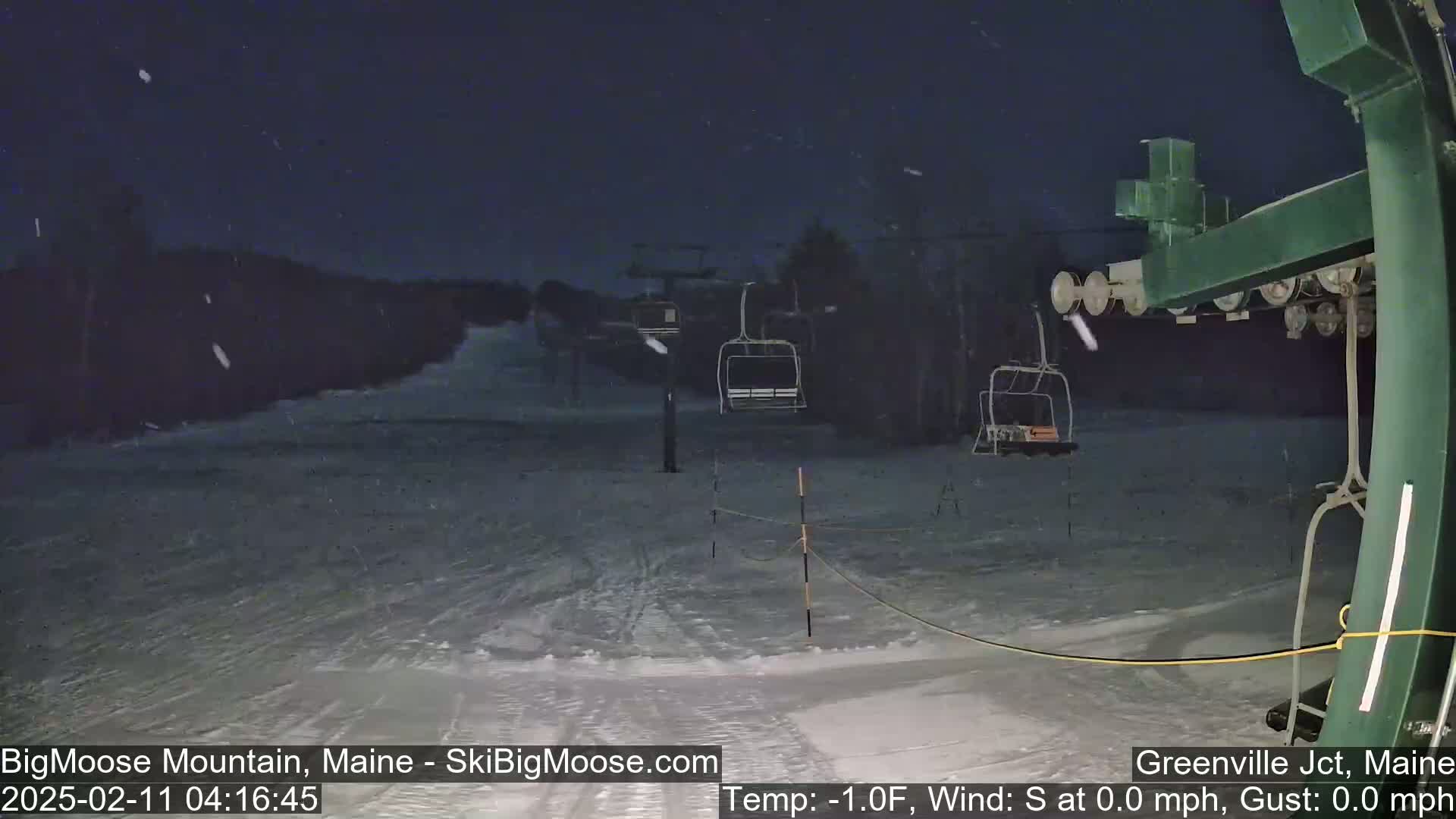 A nighttime snow flurry falls on a snow-covered ski slope with empty chairlifts visible.