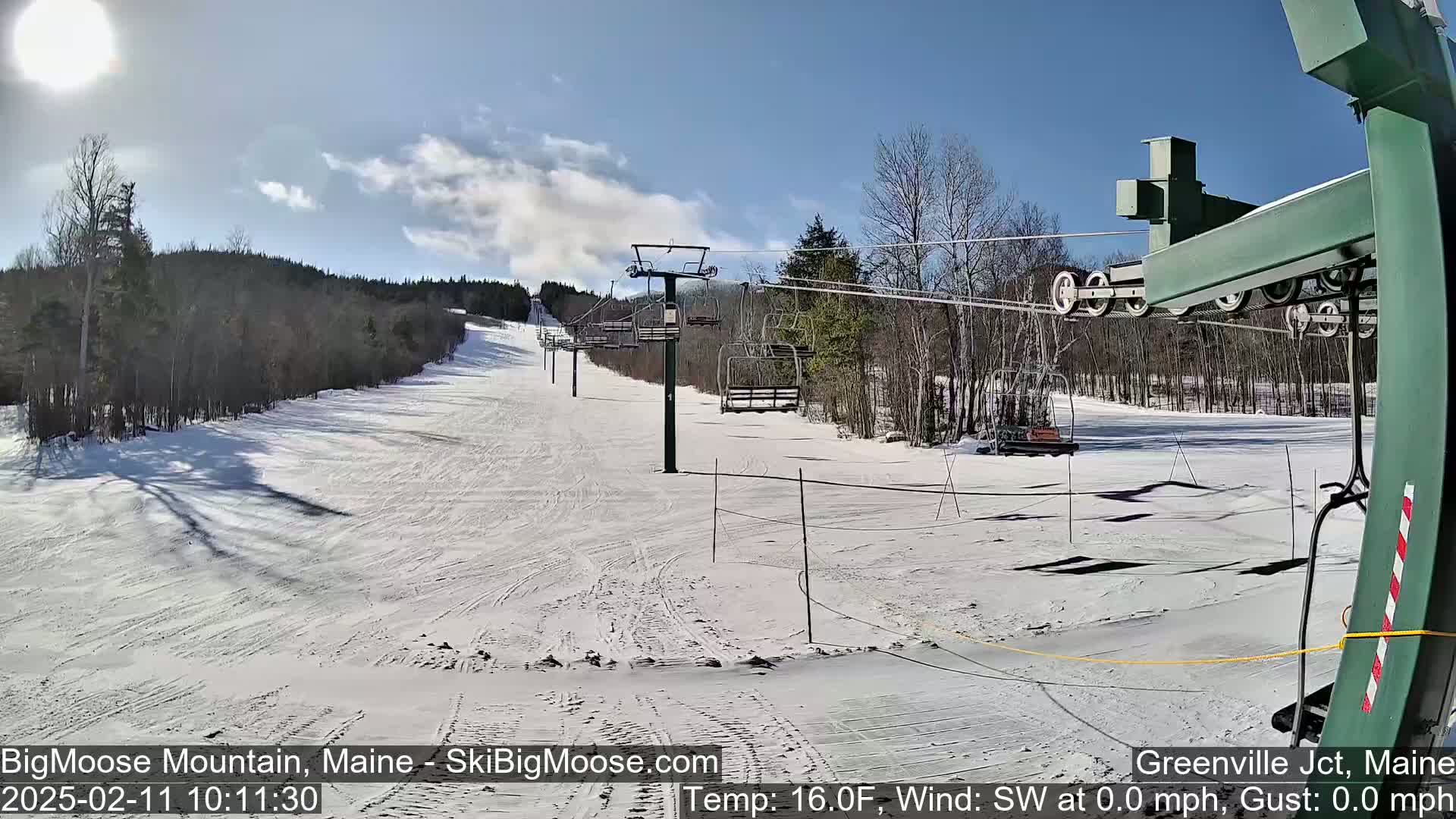 A sunny day at a snow-covered ski resort shows a chairlift and several empty chairs against a backdrop of snow-covered trees.