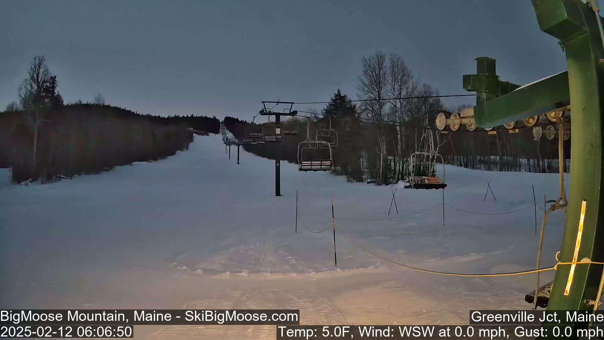 A ski lift ascends a snow-covered slope under a twilight sky.