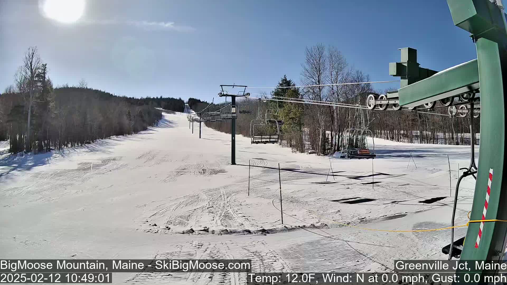 A sunny, snow-covered ski slope with a chairlift and several empty chairs.