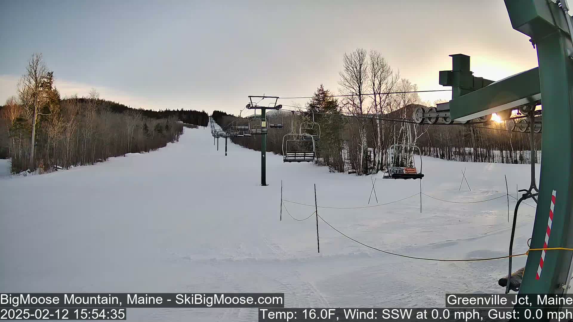 A ski lift ascends a snow-covered slope at sunset, with calm, clear weather.