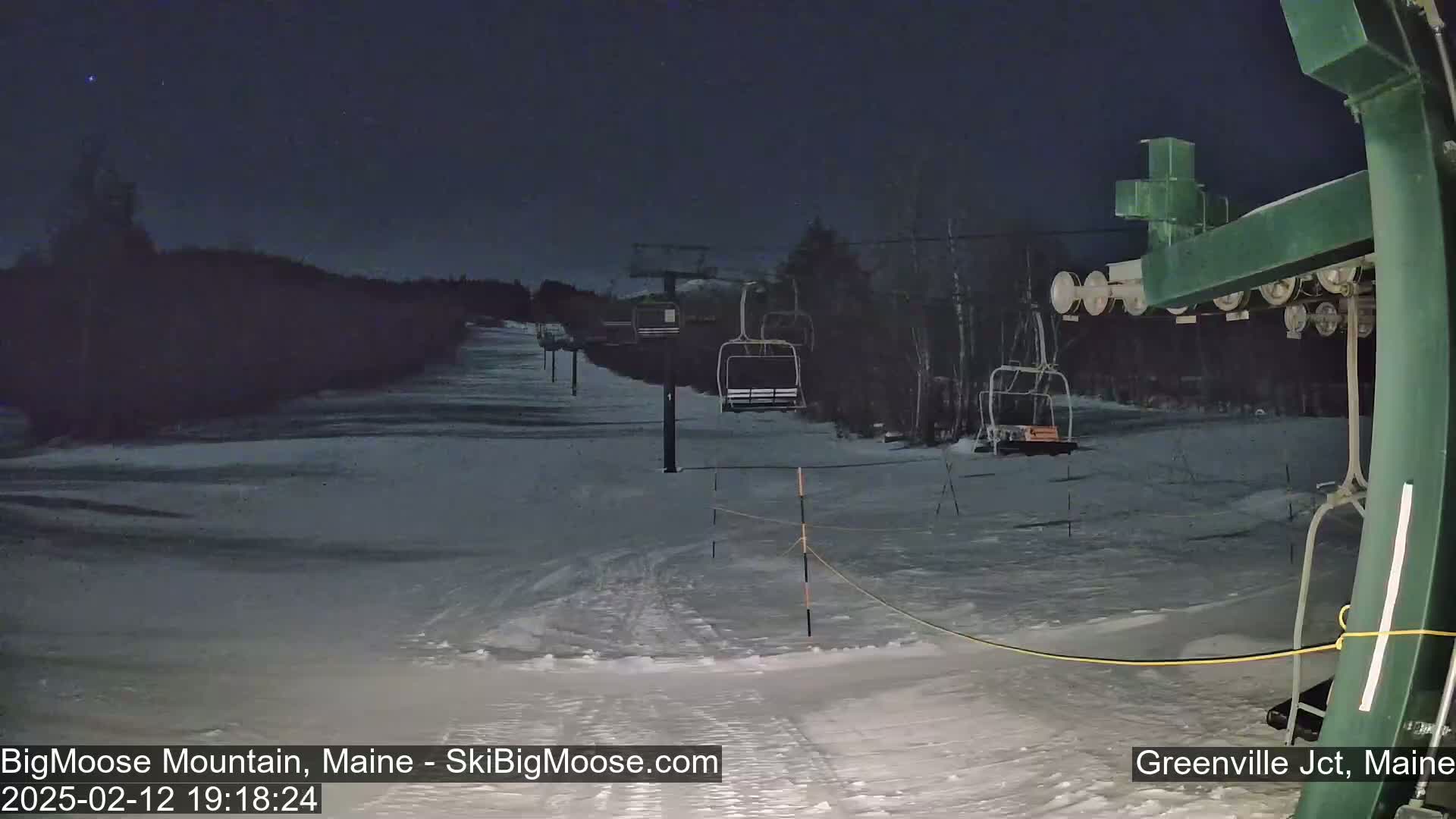 A nighttime view of a snow-covered ski slope with several empty chairlifts under a clear, dark sky.