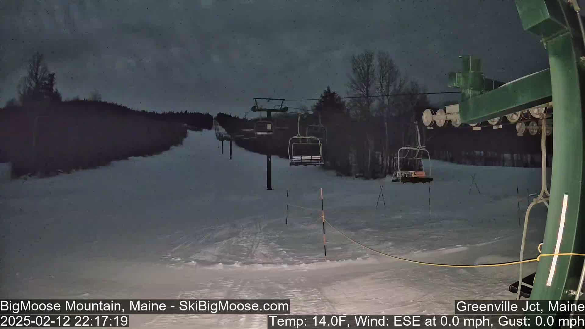 A nighttime view of a snow-covered ski slope with a chairlift and dark, overcast skies.