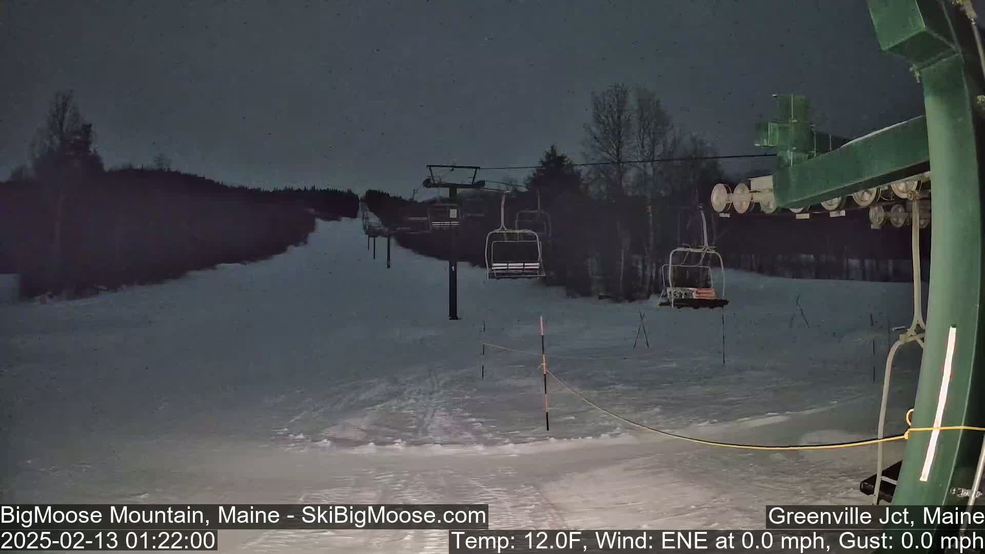 A ski lift sits on a snow-covered slope under a dark, nighttime sky.