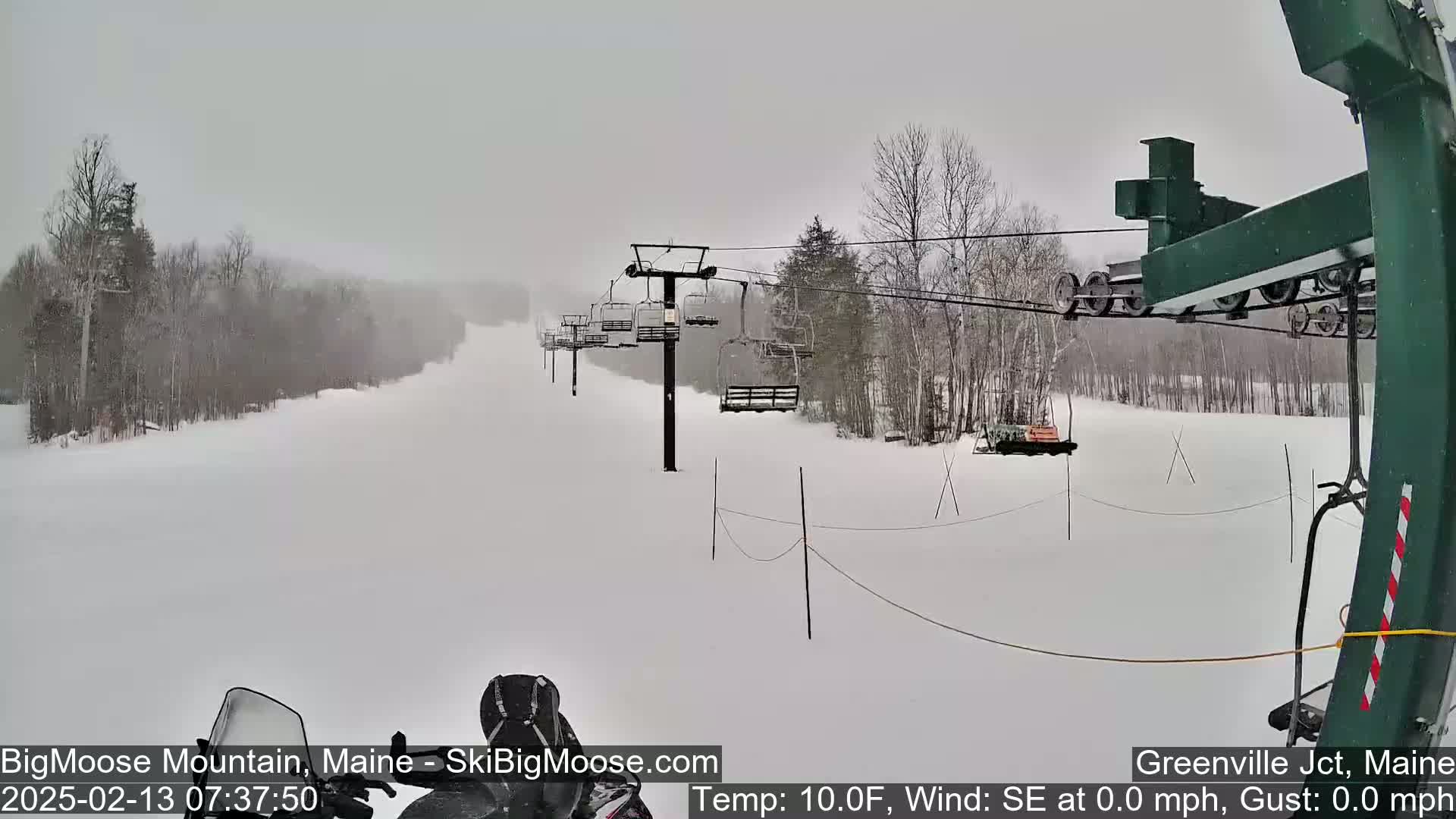 A snow-covered ski slope with a chairlift visible in the background during a snowstorm.