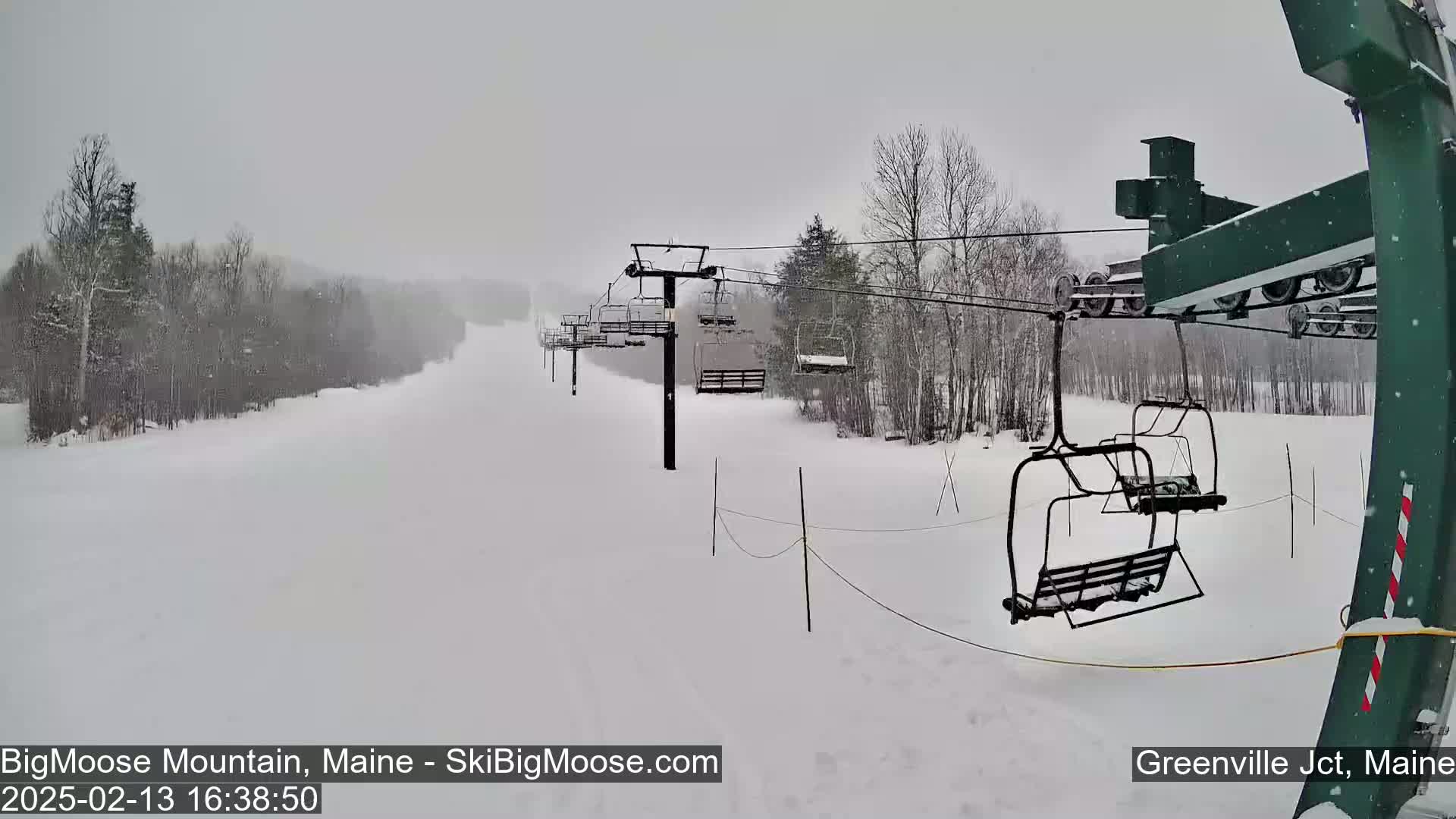 A snow-covered ski slope with a chairlift in operation during a snowfall.