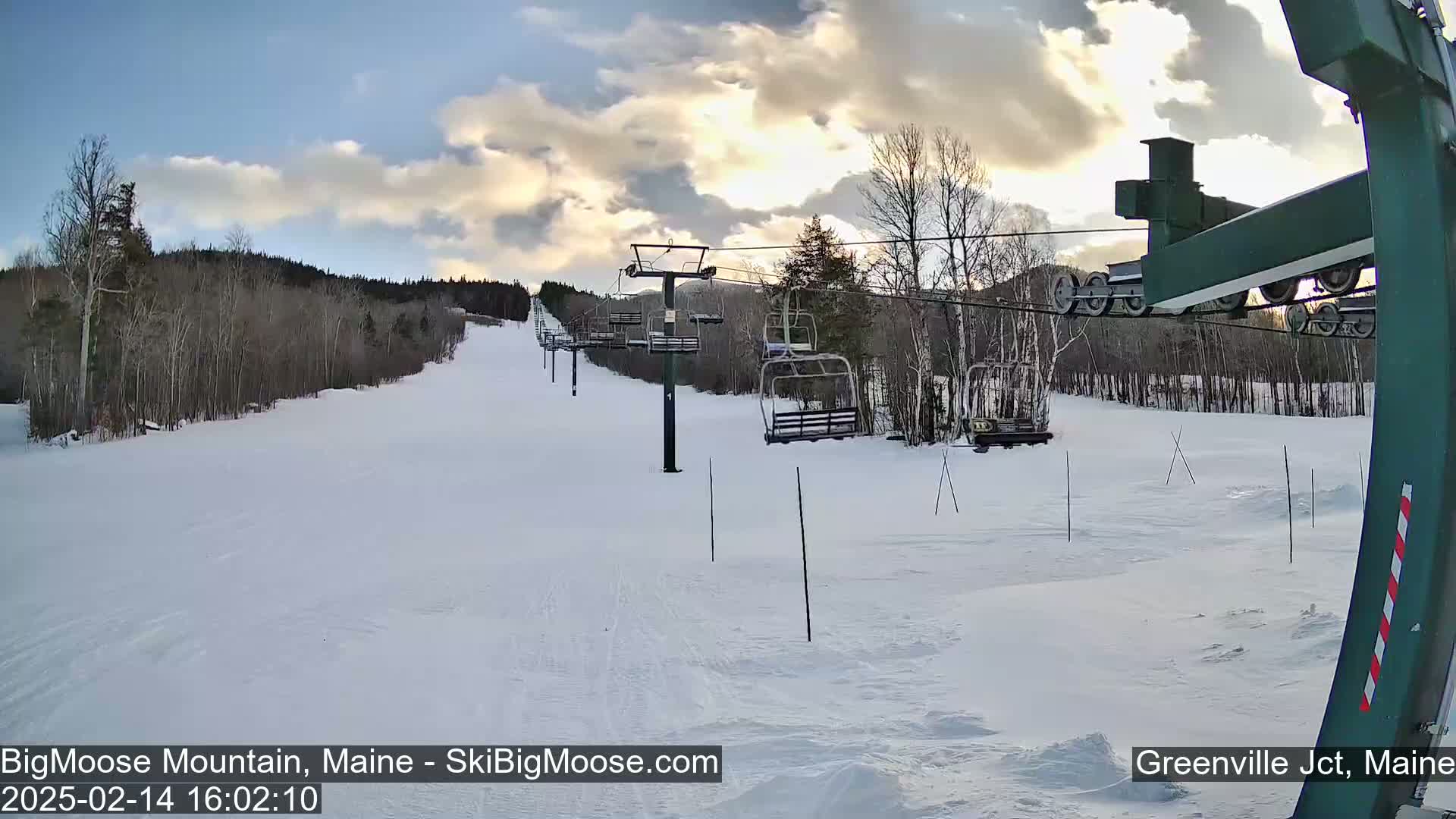 A snow-covered ski slope with a chairlift under a partly cloudy sky.