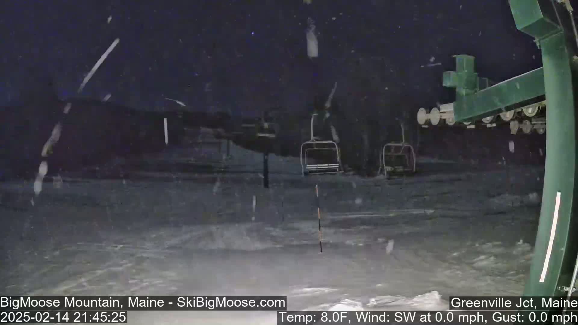 A nighttime view of a snow-covered ski slope with a chairlift and falling snow.