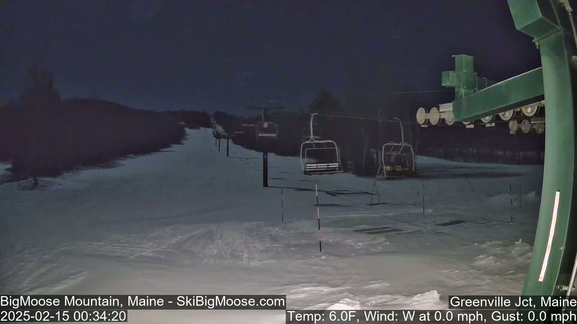 A nighttime view of a snow-covered ski slope with several empty chairlifts under a dark sky.