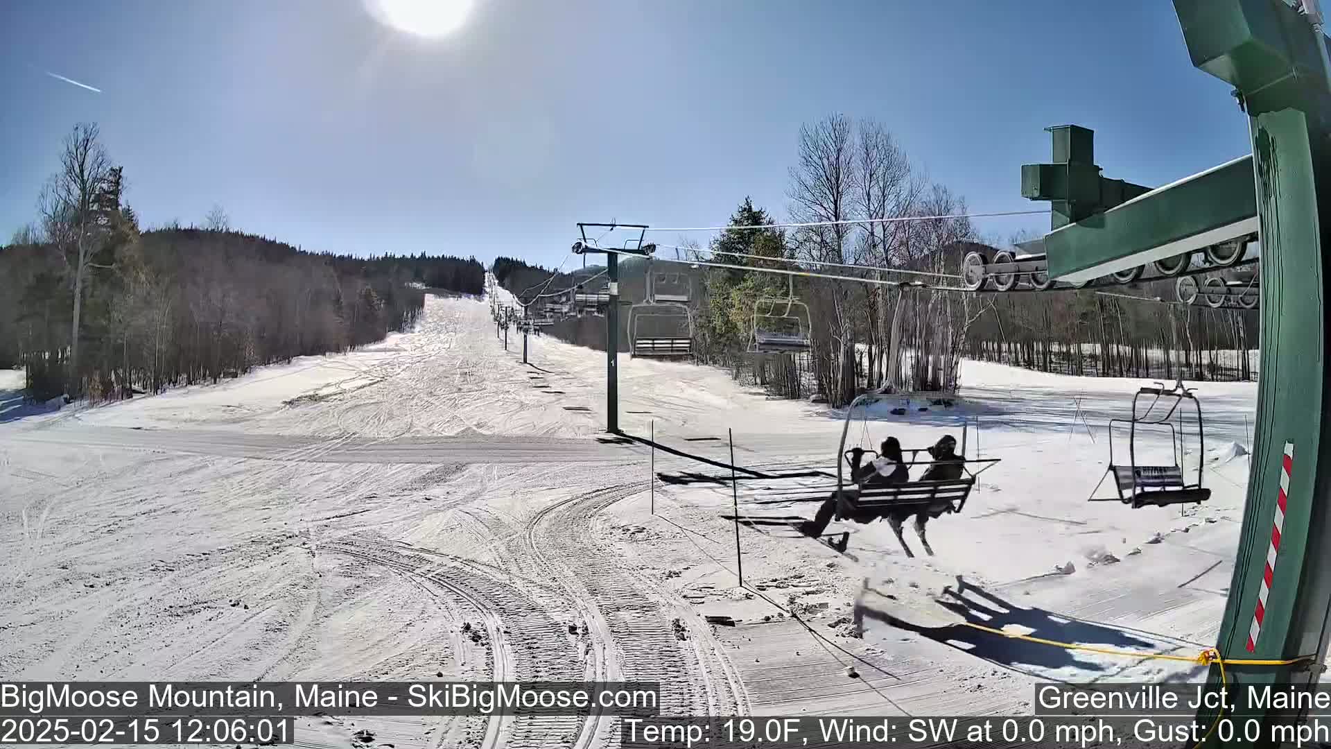 A sunny day at a snow-covered ski resort shows a chairlift with people riding it and several empty chairs ascending a mountain slope.