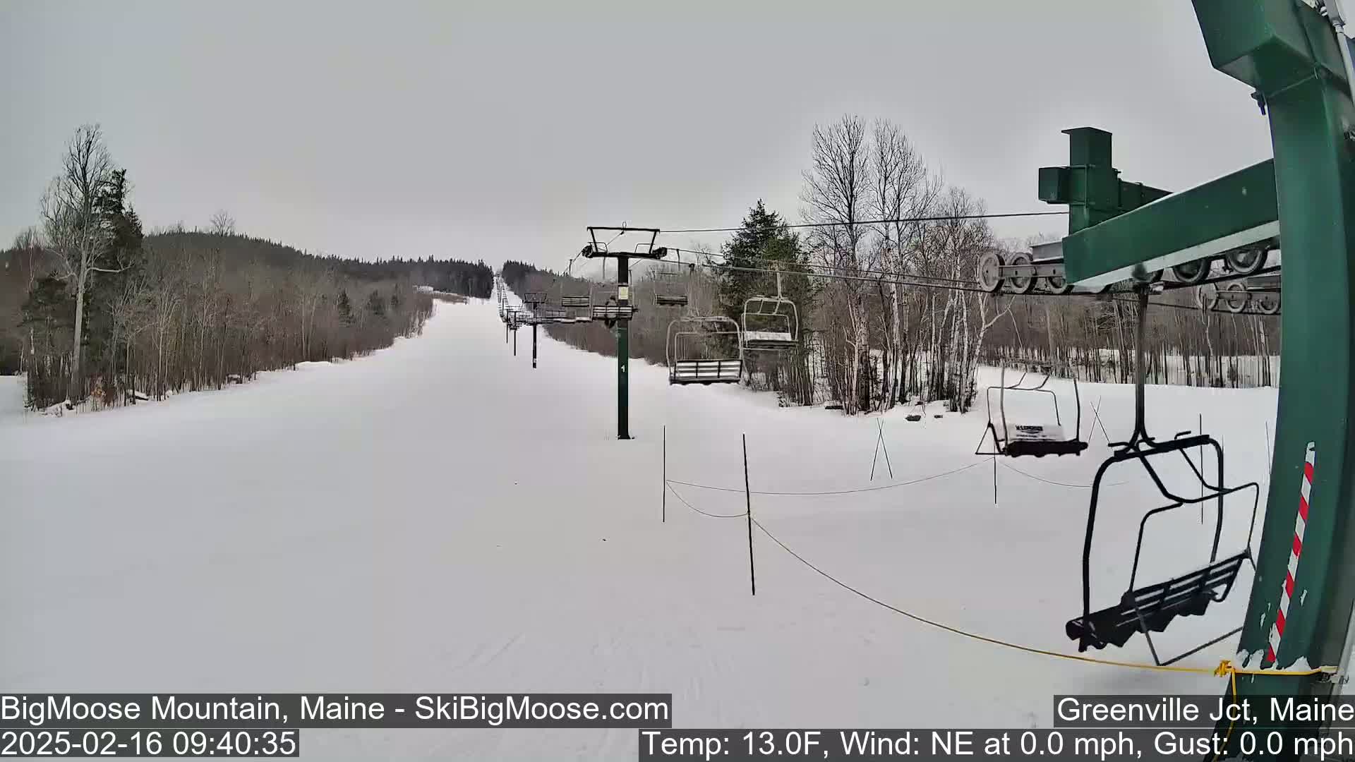 A snow-covered ski slope with a chairlift and sparsely wooded areas under a cloudy sky.