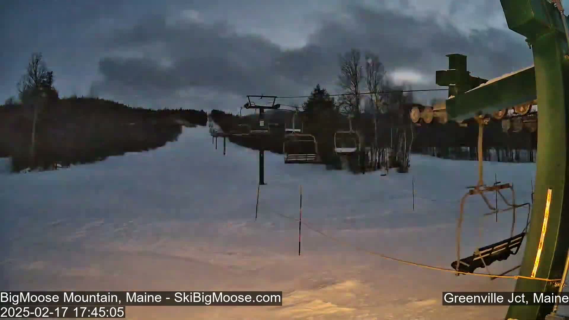 A ski lift sits on a snow-covered hill under a cloudy, dusky sky.