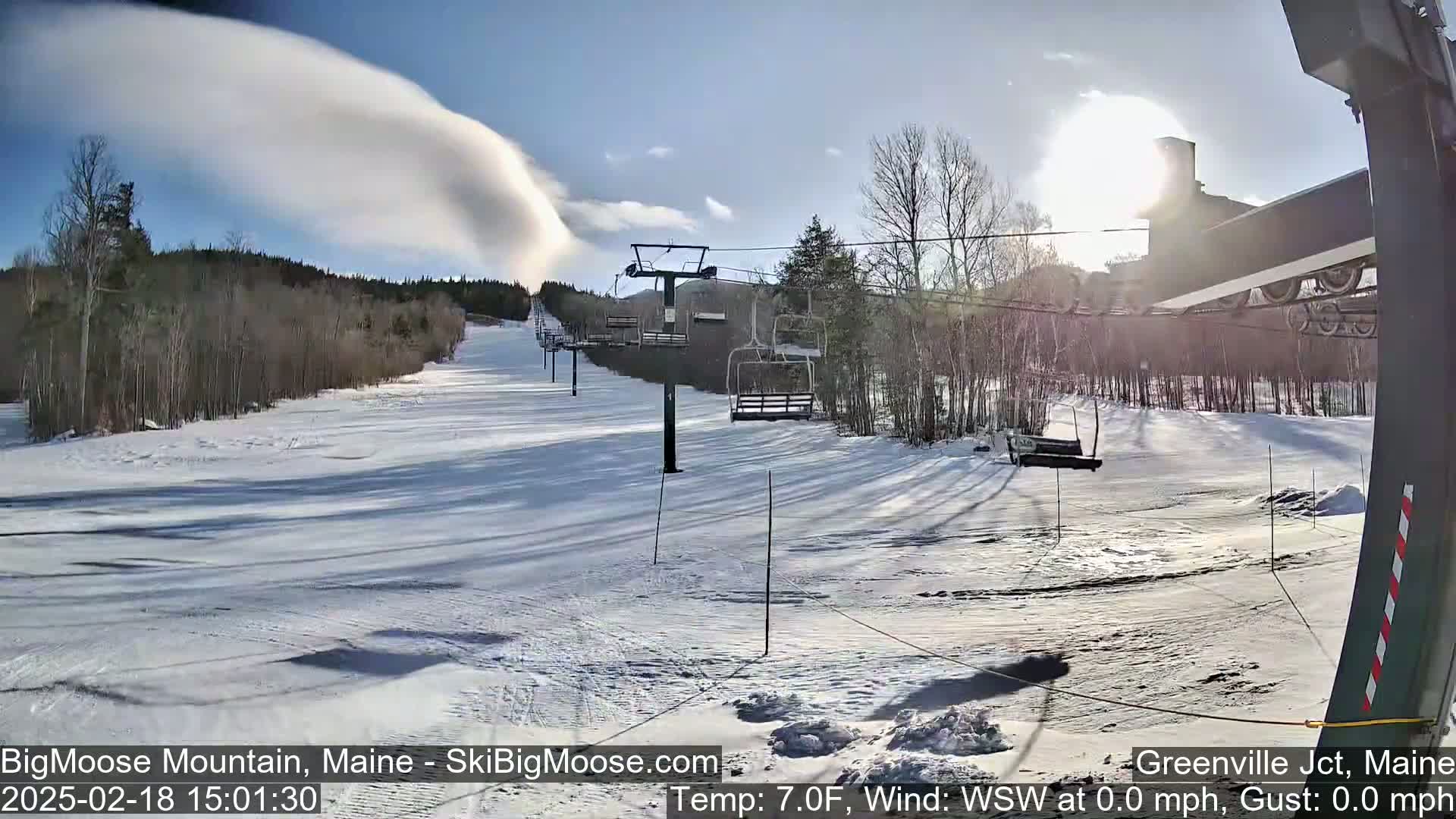 A sunny, snow-covered ski slope with a chairlift and a lenticular cloud formation in the sky.
