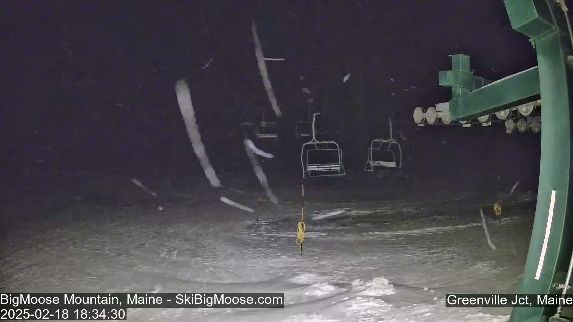 A nighttime view of a ski lift with empty chairlifts under heavy snowfall.