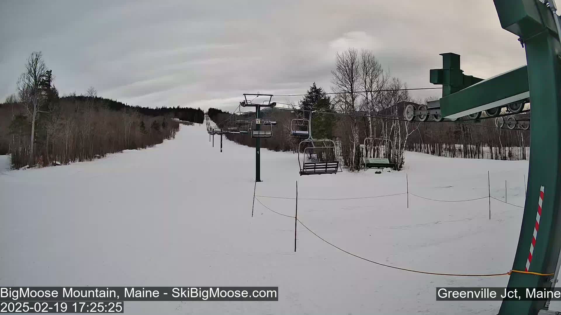 A snow-covered ski slope with a chairlift and bare trees under a cloudy sky.