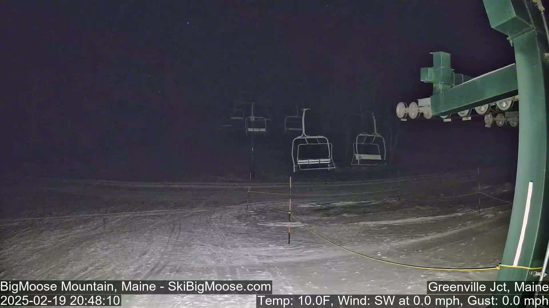 Under a dark, clear night sky, several empty chairlifts stand on a snow-covered ski slope.