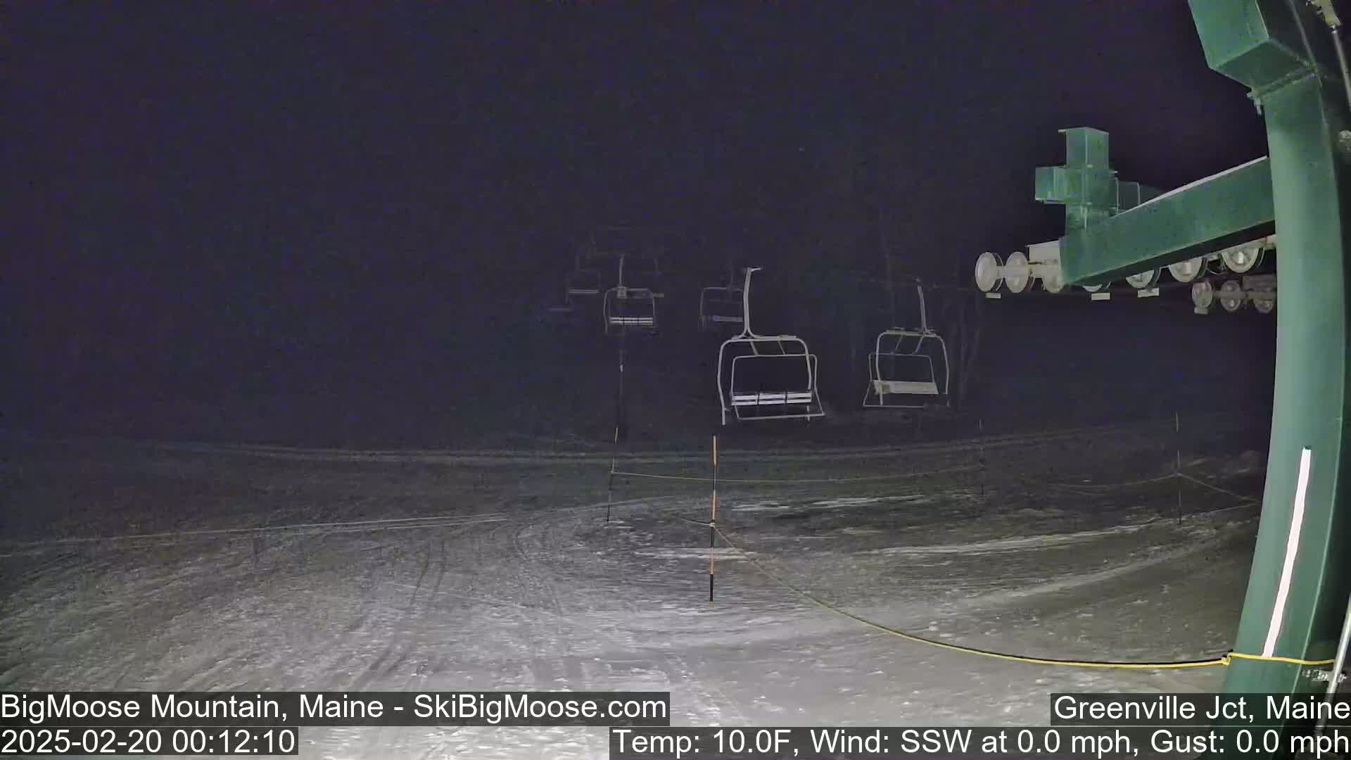 A nighttime view of a snow-covered ski lift with several empty chairs, under a dark sky.