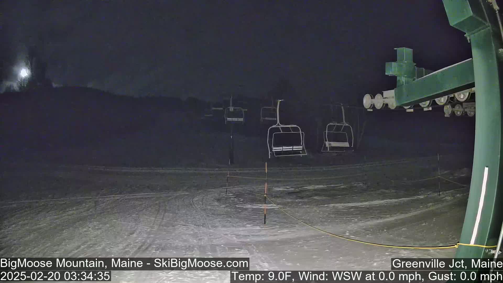 A nighttime view of a snow-covered ski slope with empty chairlifts under a dark sky.